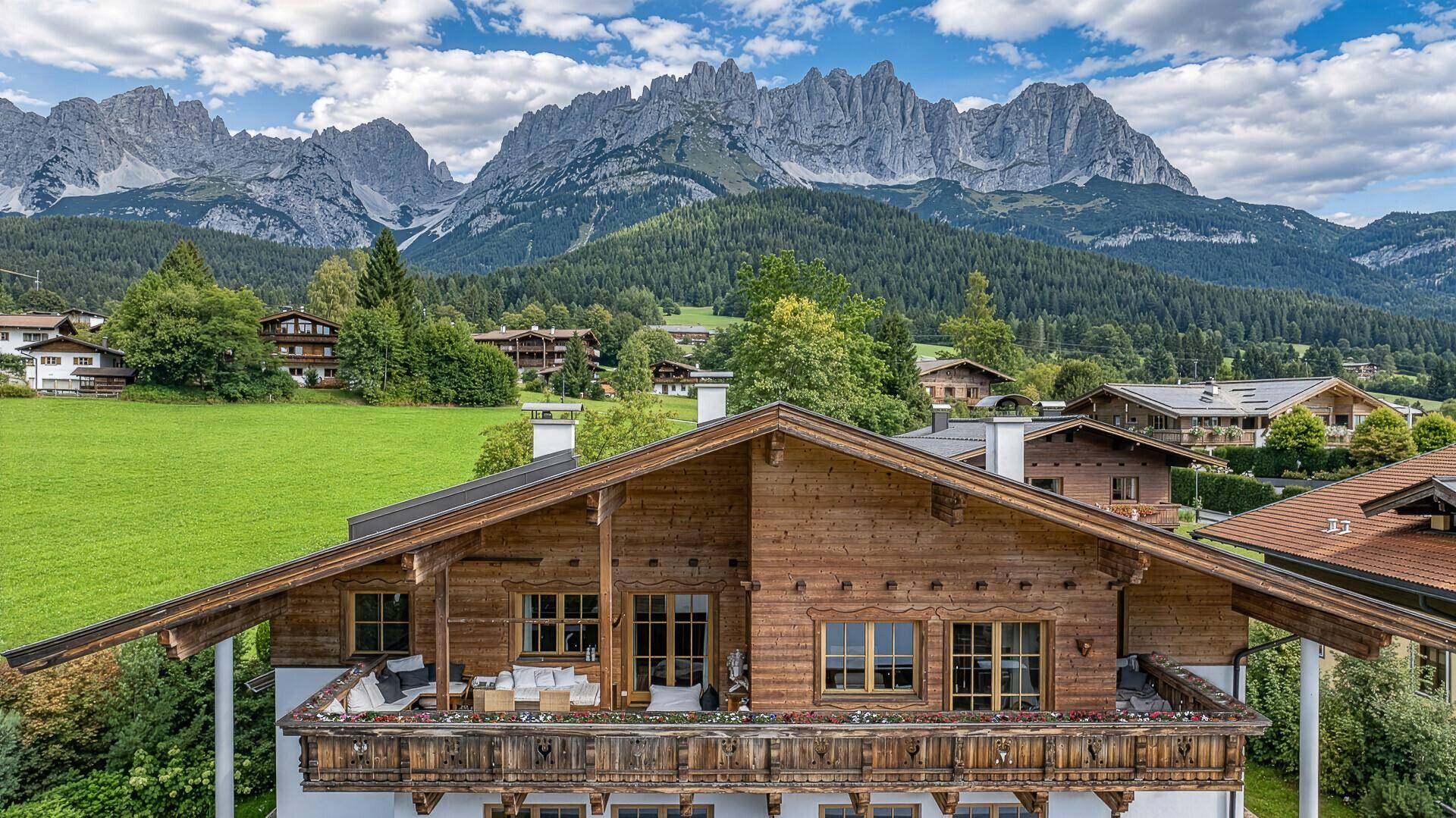Traditionelles Holzhaus mit großem Balkon und beeindruckendem Panorama der Alpen.