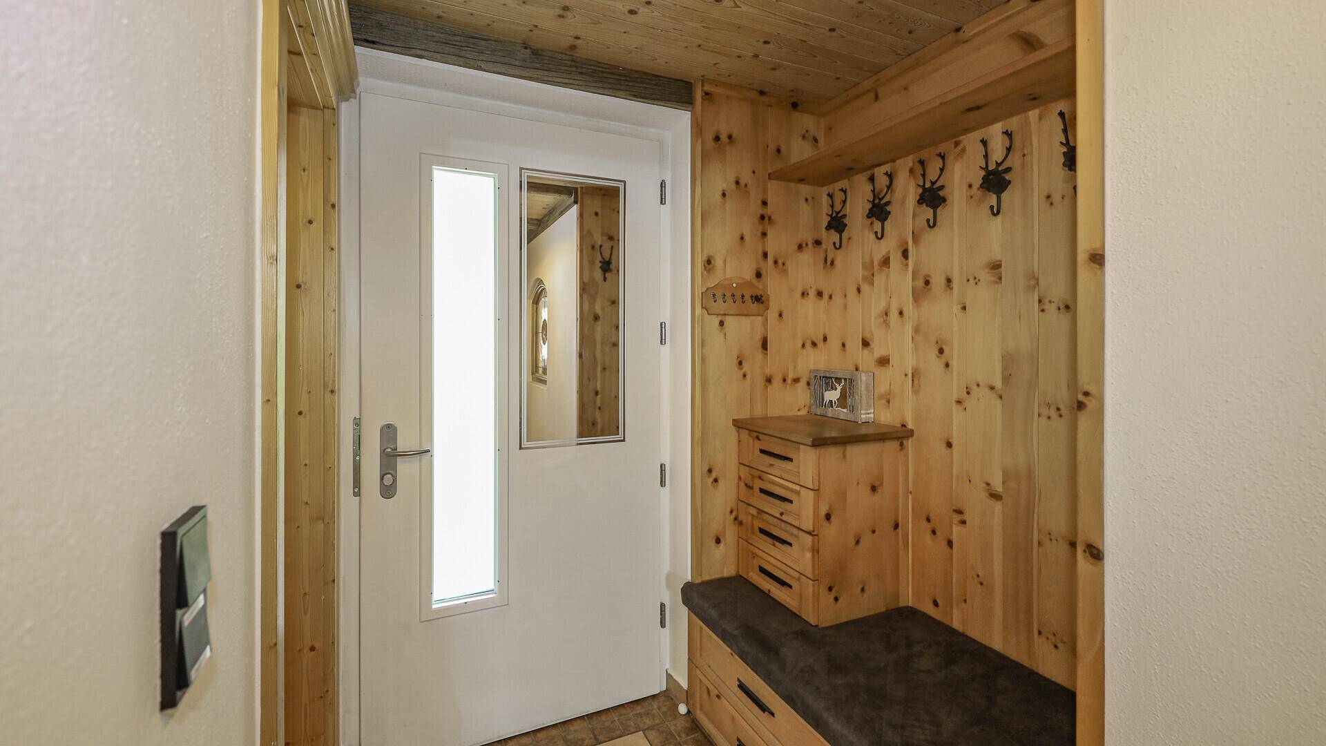 Eingangsbereich mit Holztäfelung, Sitzbank und Garderobe im rustikalen Stil.