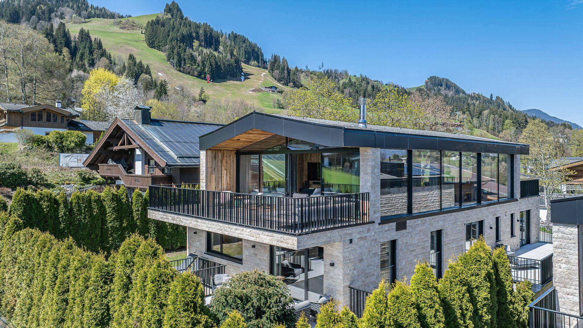 Moderne Villa mit Holzverkleidung, großen Glasfronten und weitem Blick auf die grüne Berglandschaft.
