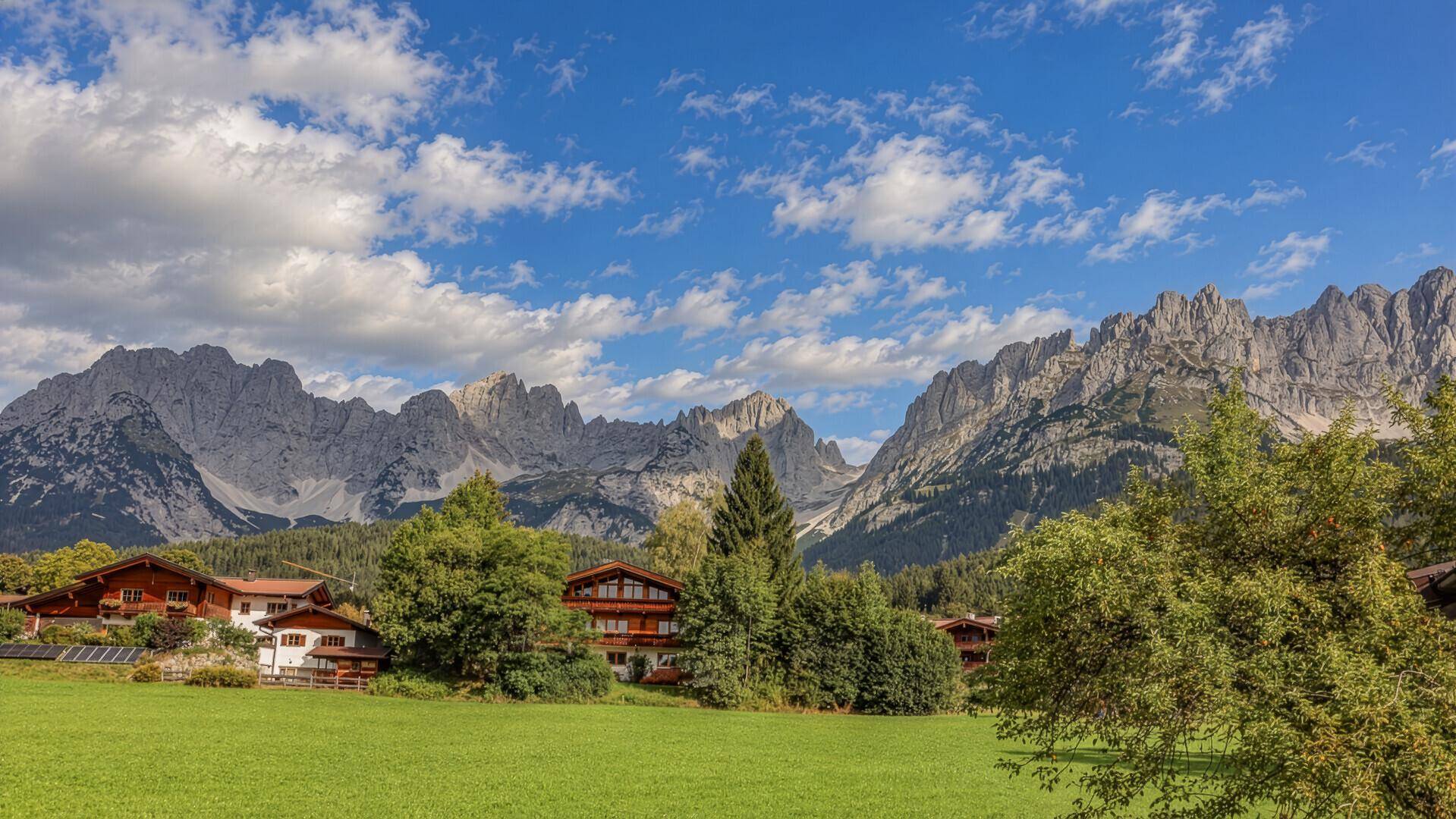 Idyllische Landschaft mit majestätischen Bergen, grünen Wiesen und traditionellen Häusern.