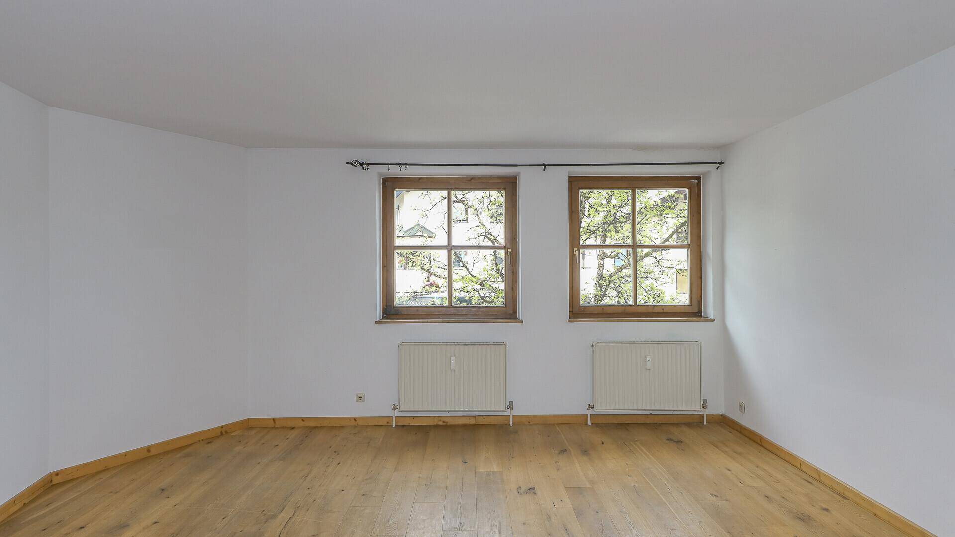 Helles, leeres Schlafzimmer mit Holzboden und zwei Fenstern, bereit zur individuellen Gestaltung.