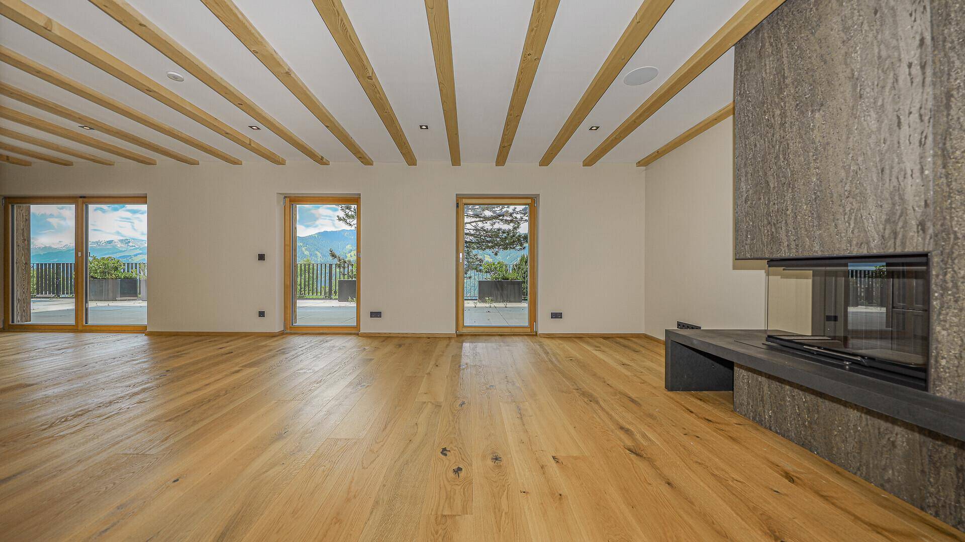 Geräumiger Wohnbereich mit modernem Kamin, Holzbalkendecke und Zugang zur Terrasse.