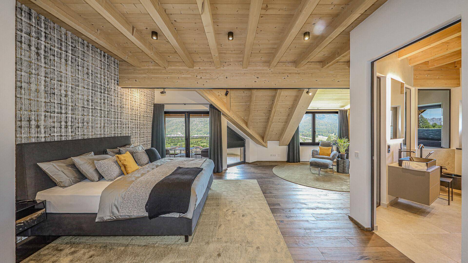 Geräumiges Schlafzimmer mit Holzbalkendecke, großem Bett und direktem Zugang zum Bad.