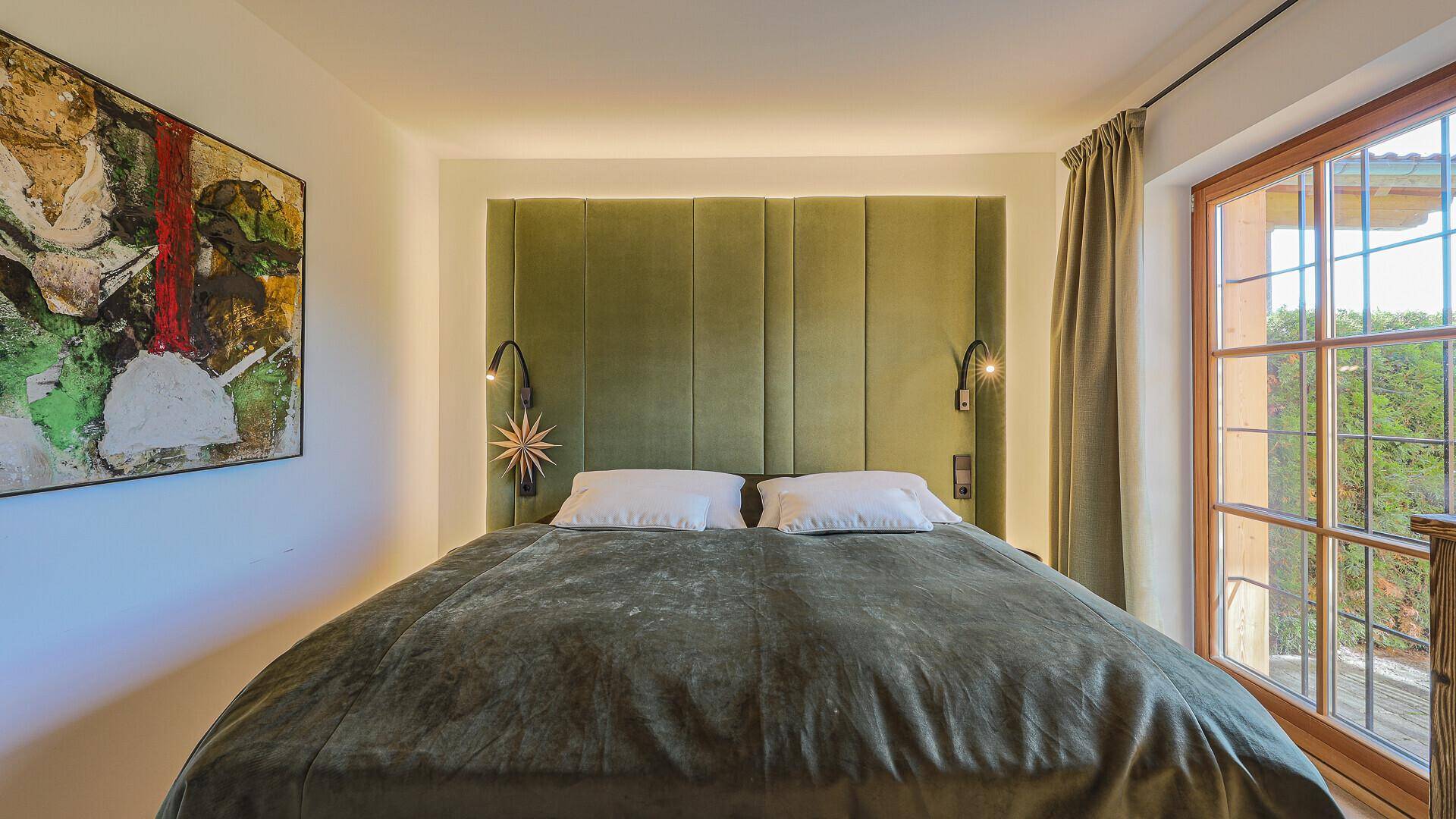 Helles Schlafzimmer mit Doppelbett, grüner Polsterwand und Fenster mit Blick ins Grüne.