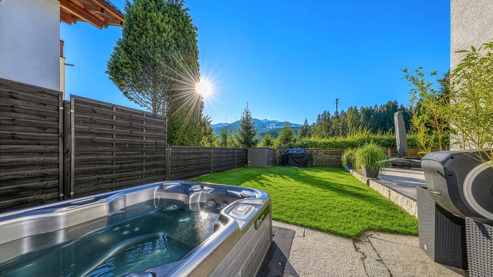 Entspannender Whirlpool-Bereich im sonnigen Garten mit Blick auf die umliegende Berglandschaft.