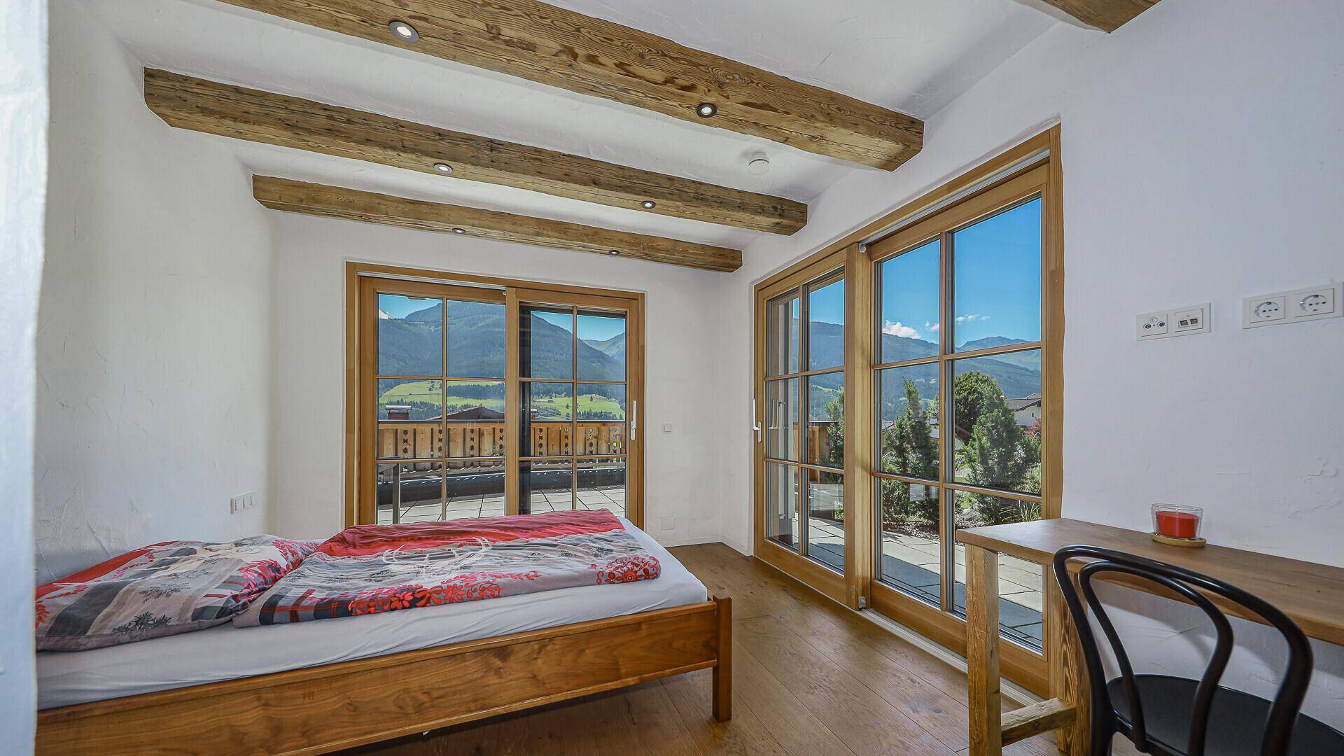 Helles Schlafzimmer mit Holzbalken, Parkettboden und Zugang zu einem Balkon mit Bergblick.