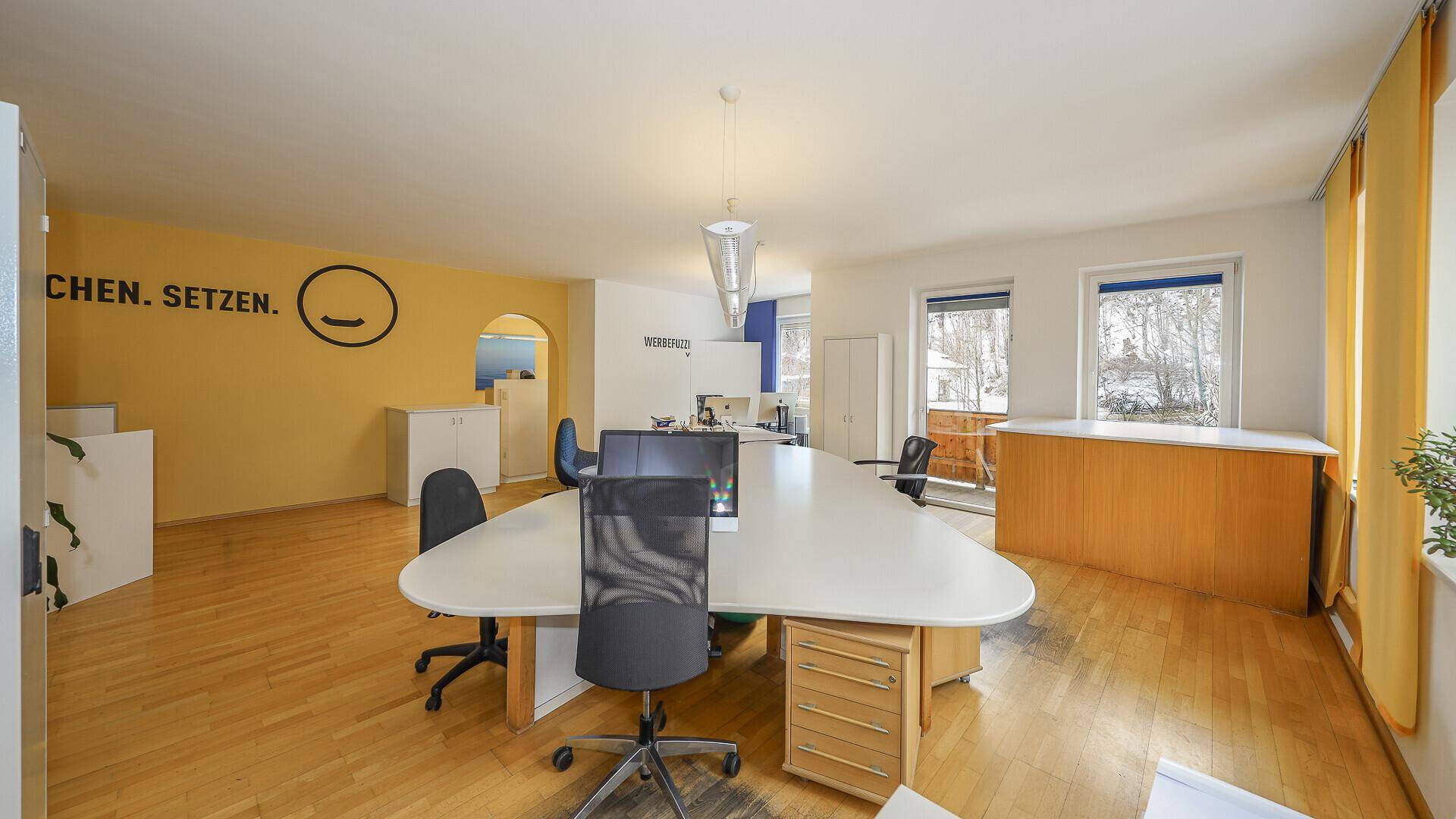 Offenes Büro mit gelben Wänden, Holzboden und mehreren Arbeitsbereichen, hell und funktional eingerichtet.