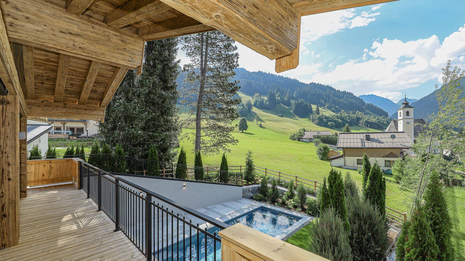 Geräumiger Holzbalkon mit Blick auf den Pool, die Berge und das malerische Tal.