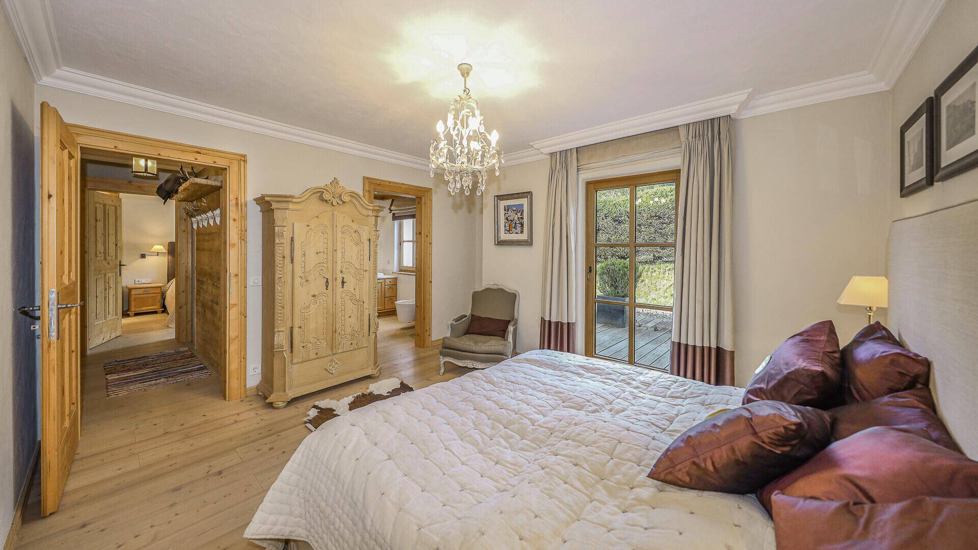 Schlafzimmer mit Holzboden, traditionellem Schrank und Zugang zu Bad und Außenbereich.