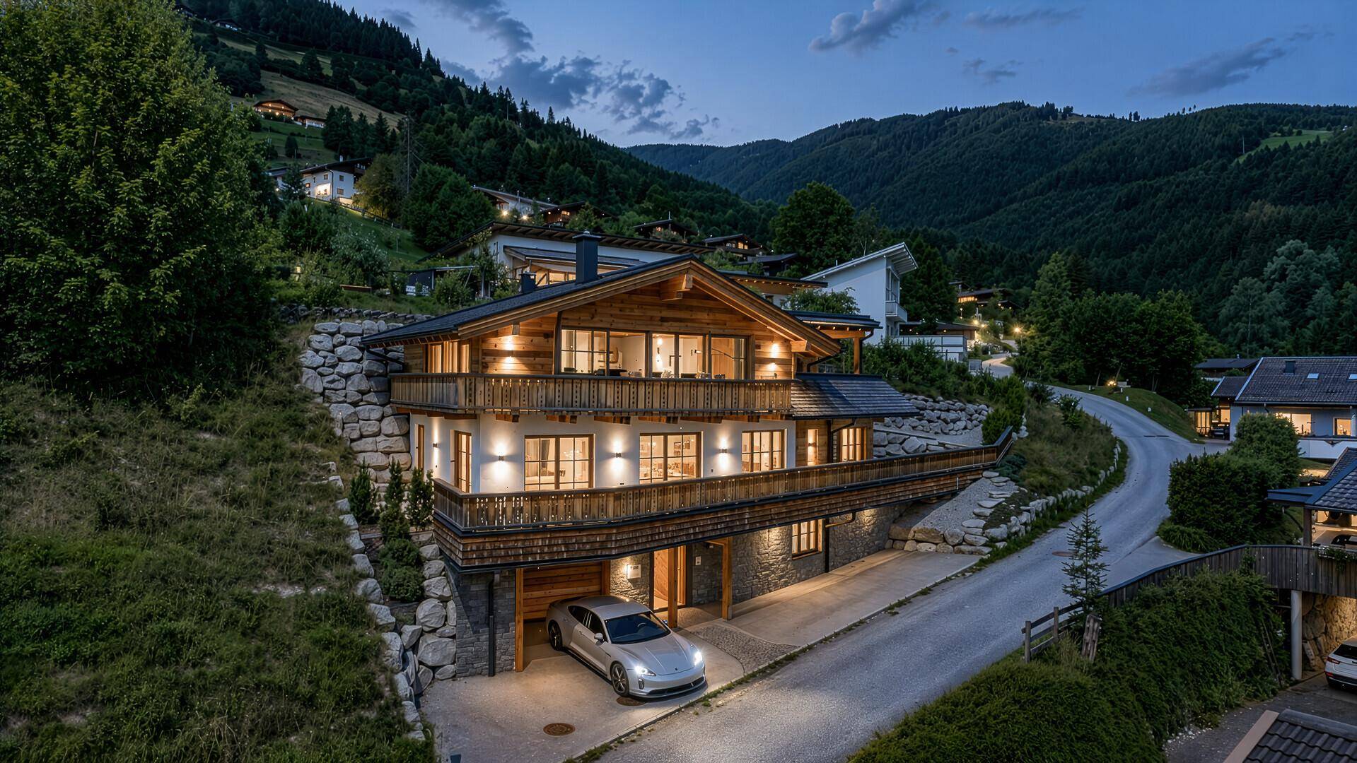 Luxuriöses Chalet in den Bergen bei Dämmerung mit warmer Beleuchtung und Panoramablick.
