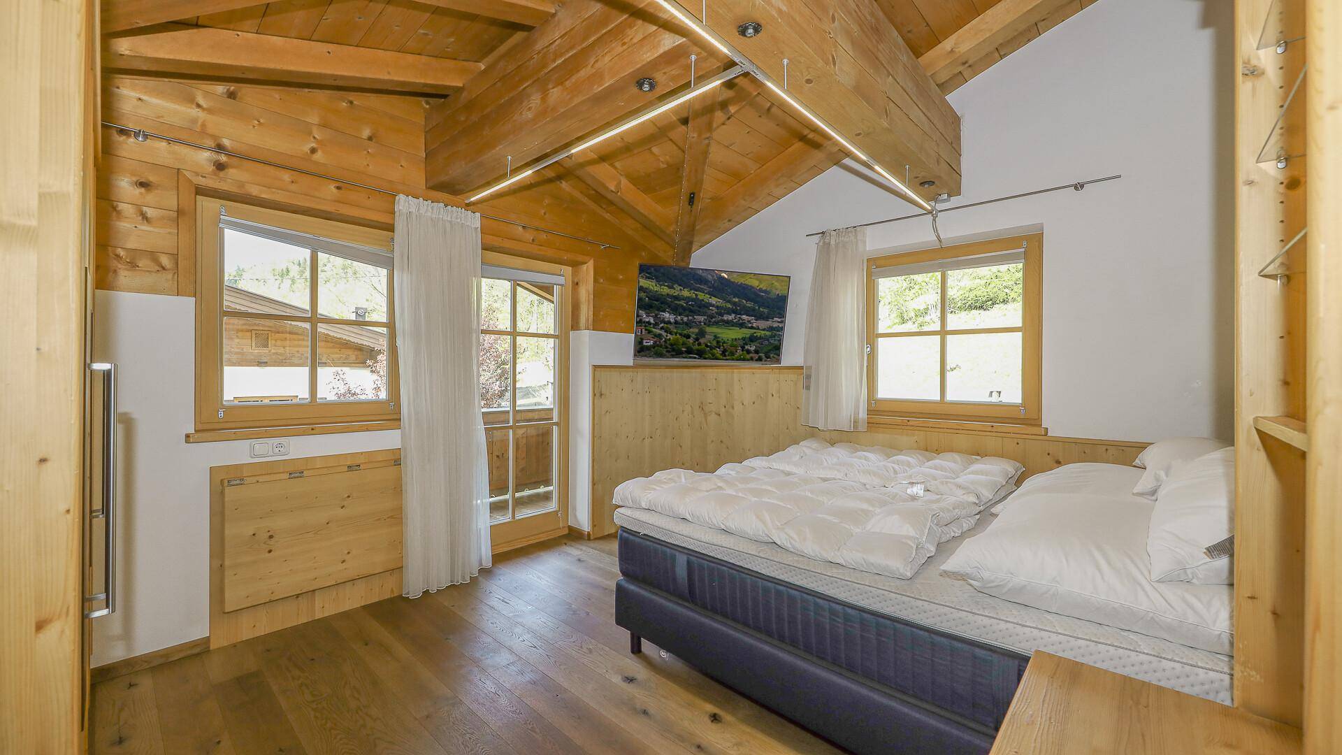 Schlafzimmer mit Holzwänden, Holzbalkendecke und einem Fernseher an der Wand.