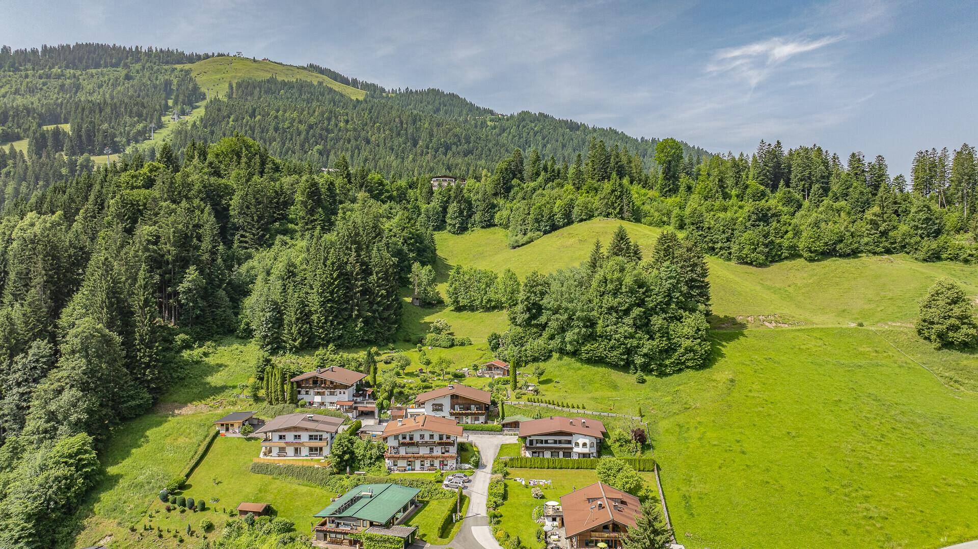 Panoramablick auf eine alpine Siedlung mit bewaldeten Bergen und Skipisten im Hintergrund.