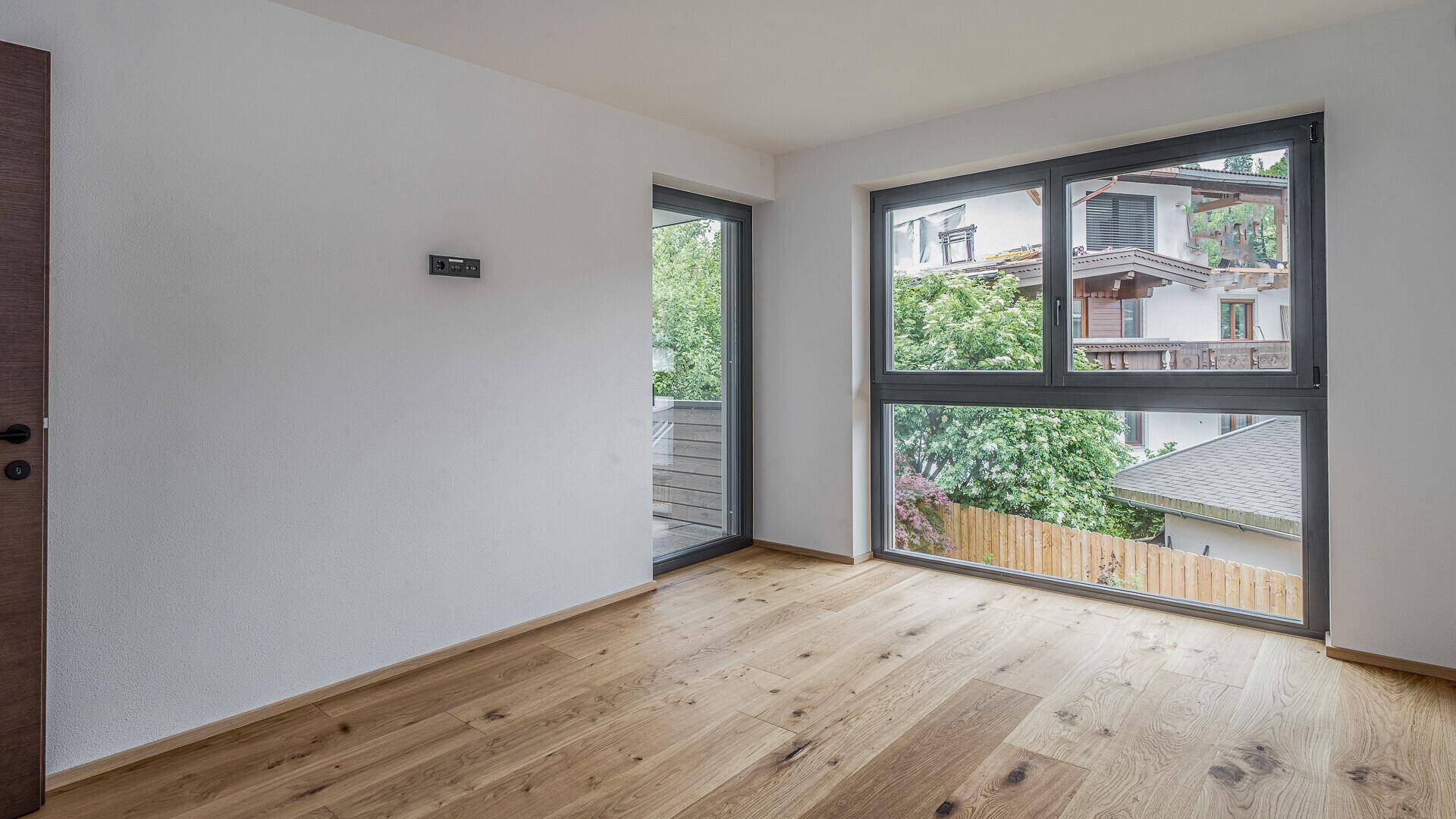 Helles Zimmer mit Holzboden, großem Fenster und direktem Zugang zu einem privaten Balkon.