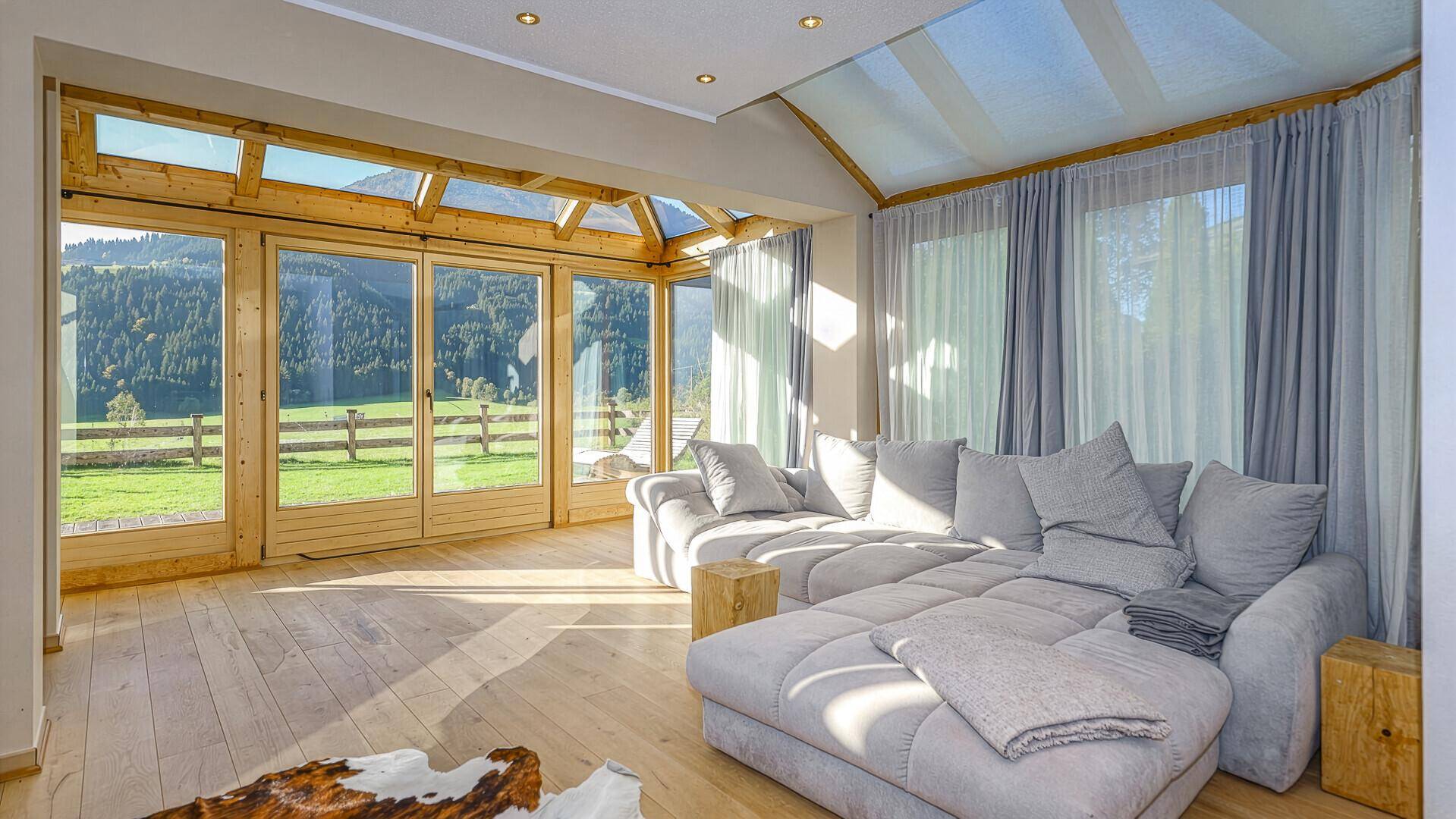 Heller Wohnbereich mit großem Ecksofa und Panoramafenstern, die einen weiten Blick auf die Berge bieten.