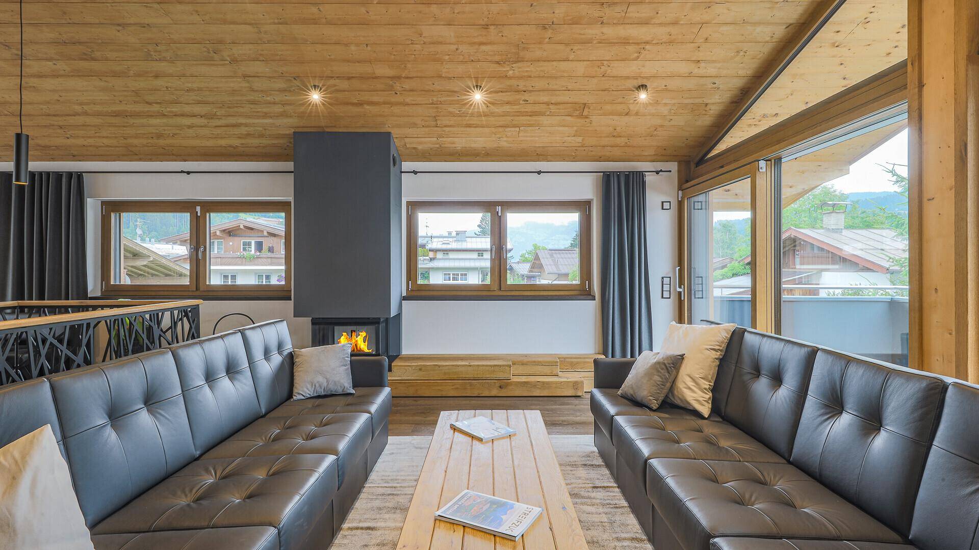 Gemütlicher Wohnbereich mit zwei Ledersofas, Holzbalkendecke und einem modernen Kamin.