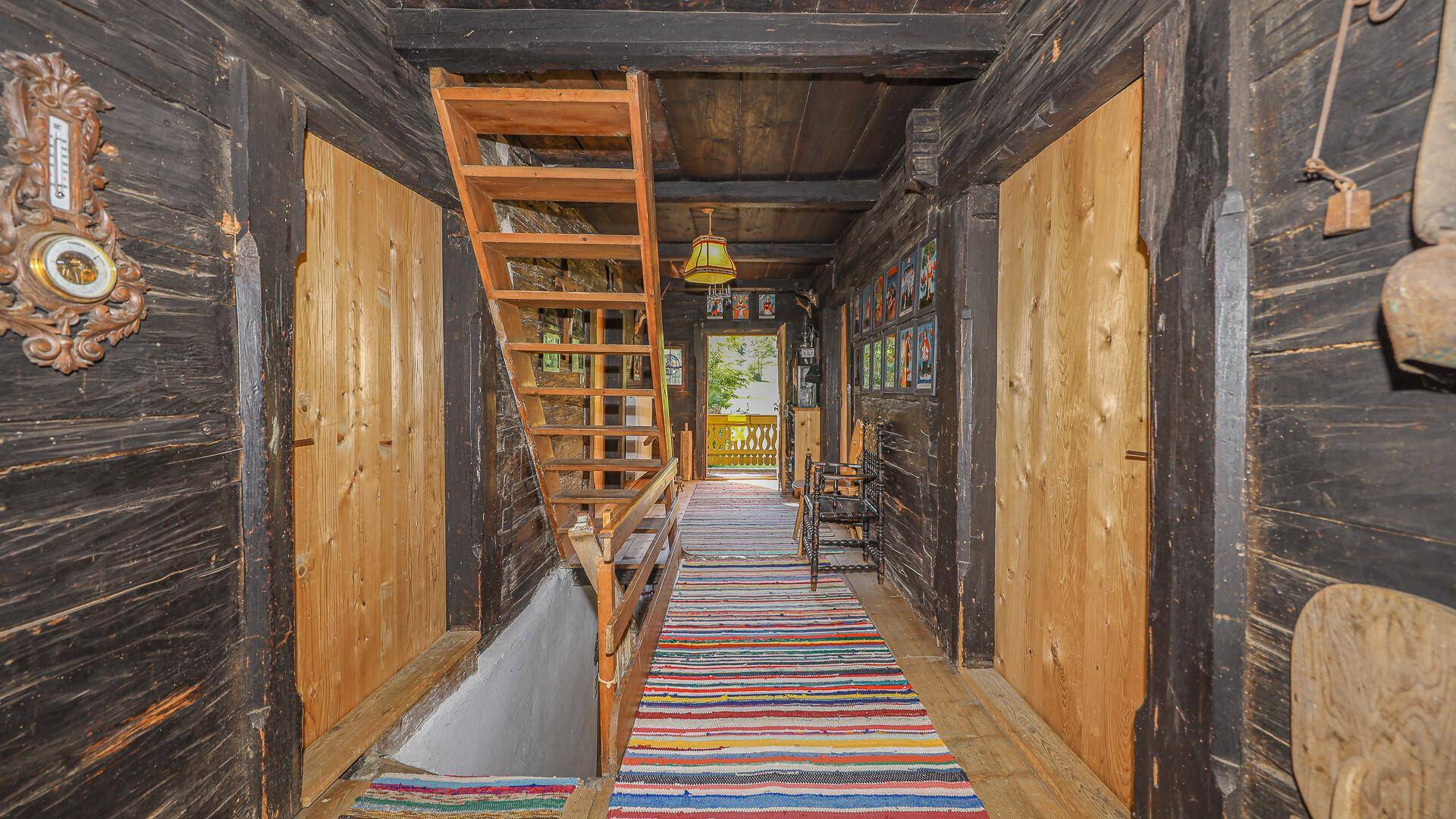 Rustikaler Flur mit Holztreppe, dunklen Holzwänden und traditionellen Teppichen.