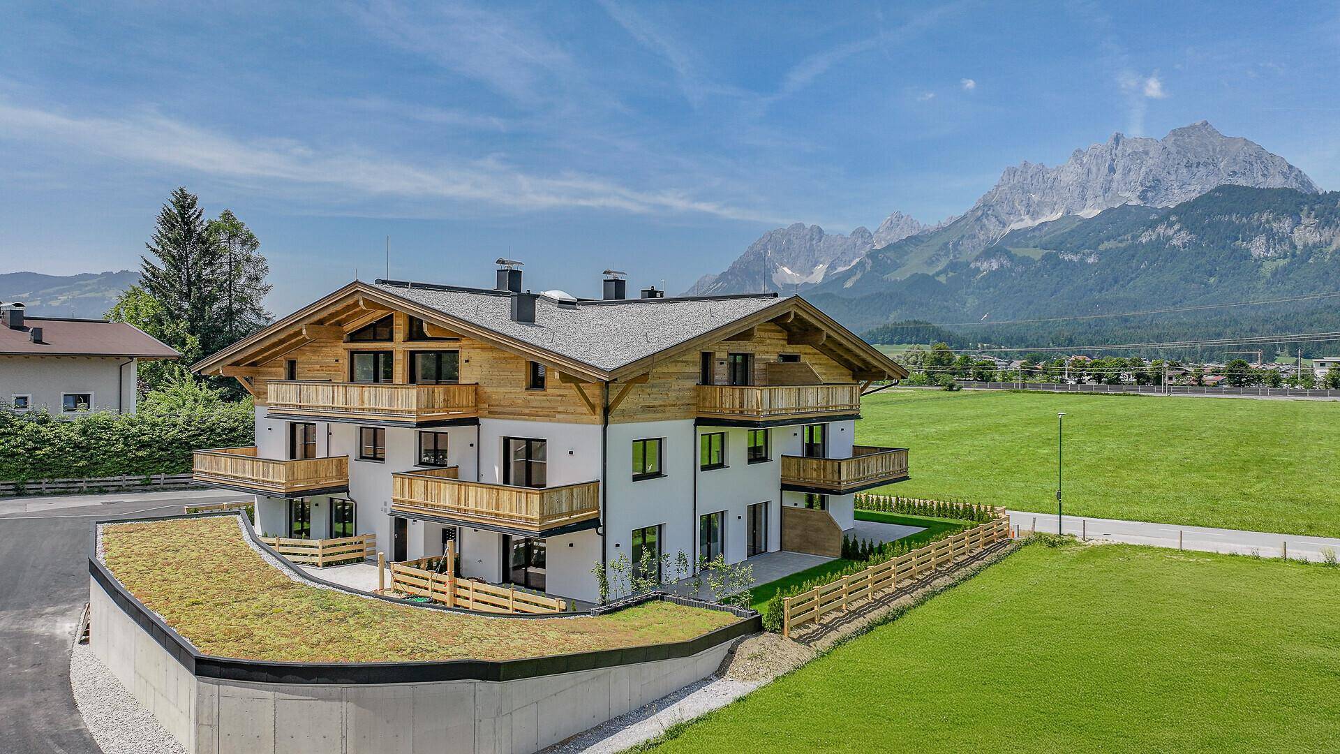 Modernes Mehrfamilienhaus im alpinen Stil mit Bergblick und Tiefgarage mit Gründach.
