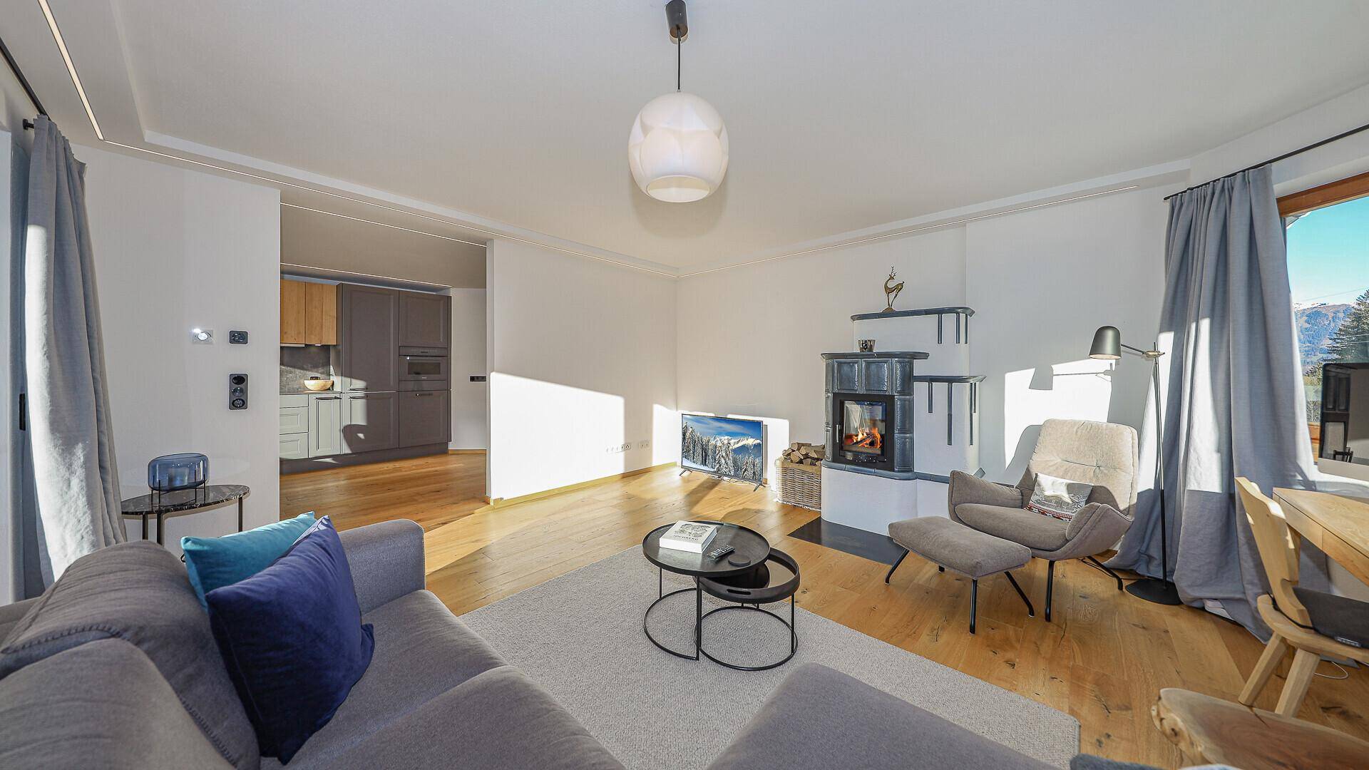 Heller Wohnbereich mit modernem Sofa, Kachelofen und offenem Übergang zur Küche.