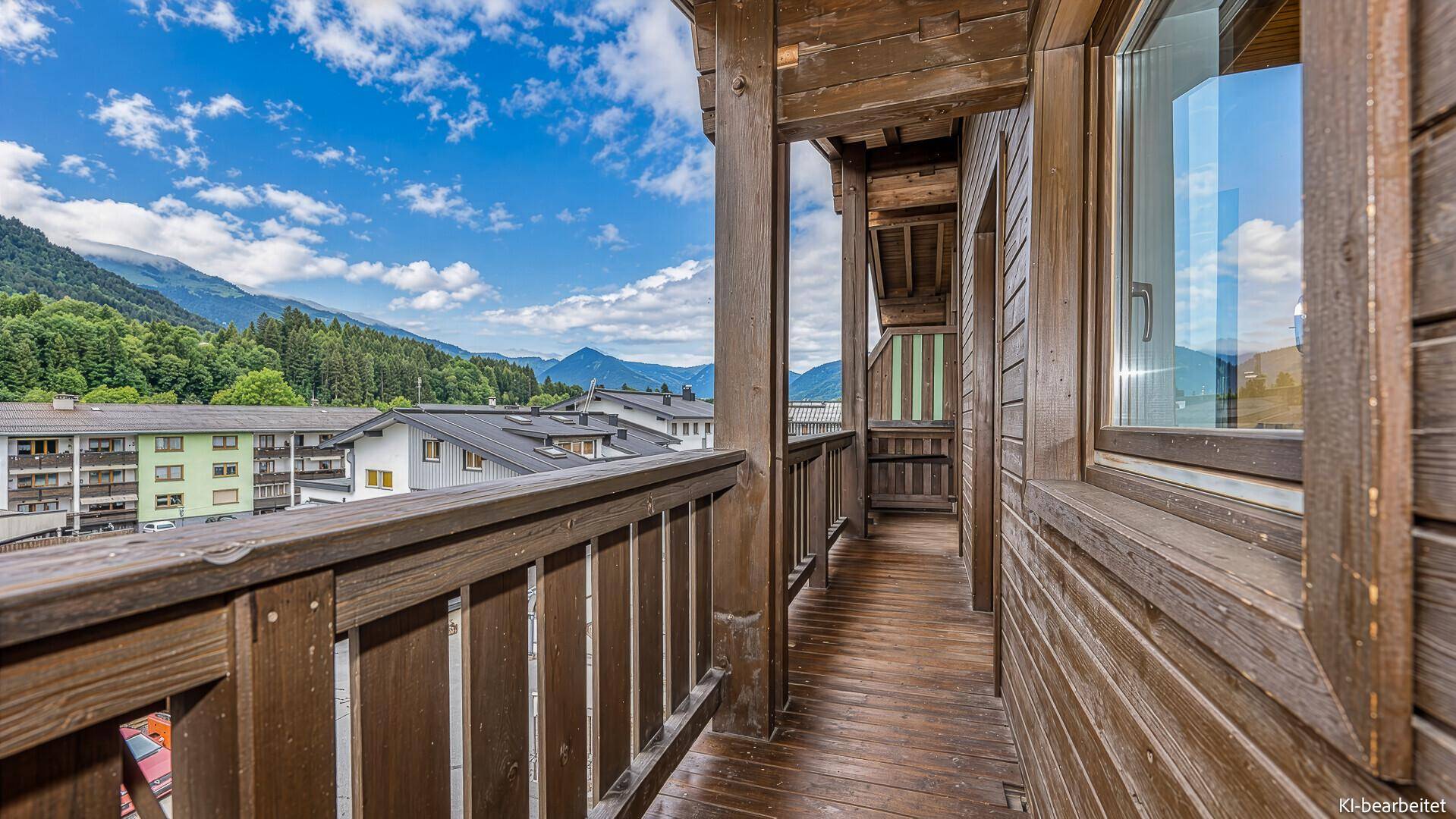 Langer Holzbalkon mit Panoramablick auf die umliegende Berglandschaft und Gebäude.