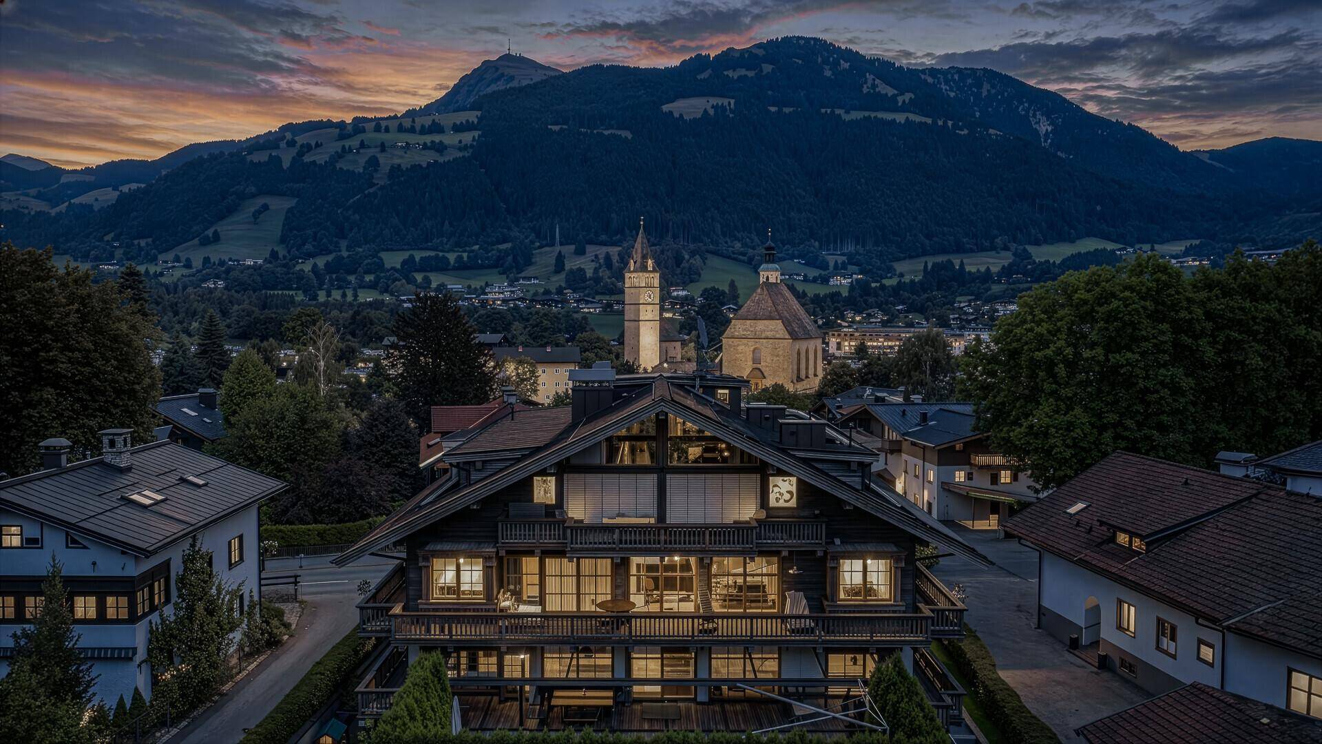 Abendlicher Panoramablick auf ein luxuriöses Gebäude in den Alpen, mit beleuchteten Fenstern und Bergsilhouette.
