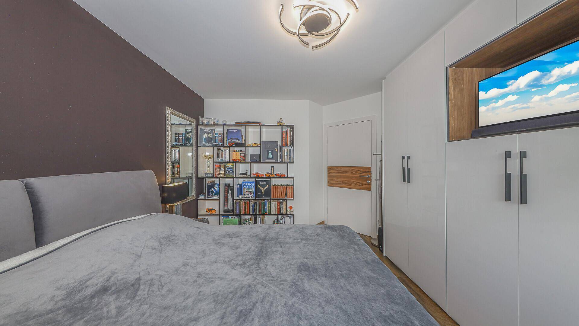 Modernes Schlafzimmer mit integriertem TV in den Einbauschränken und stilvollem Bücherregal.