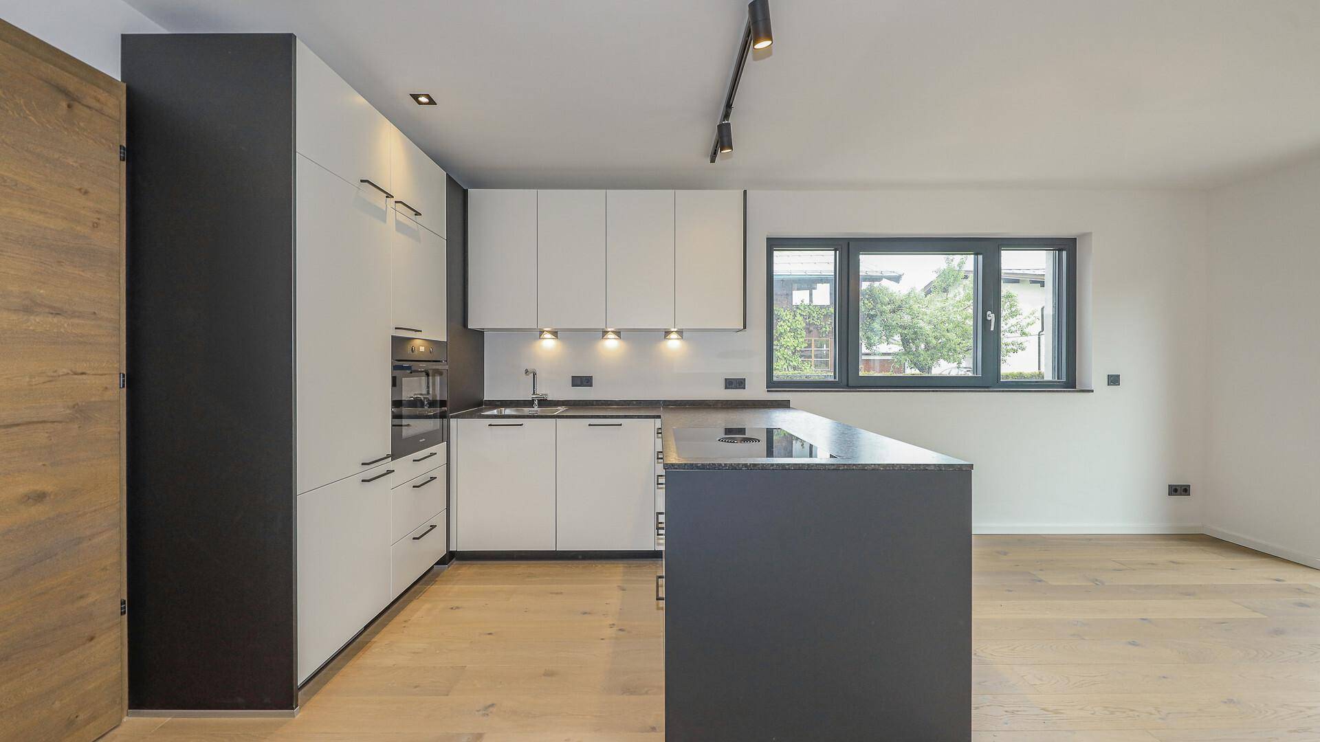 Moderne Einbauküche mit Kochinsel, weißen Schränken und dunkler Arbeitsplatte.