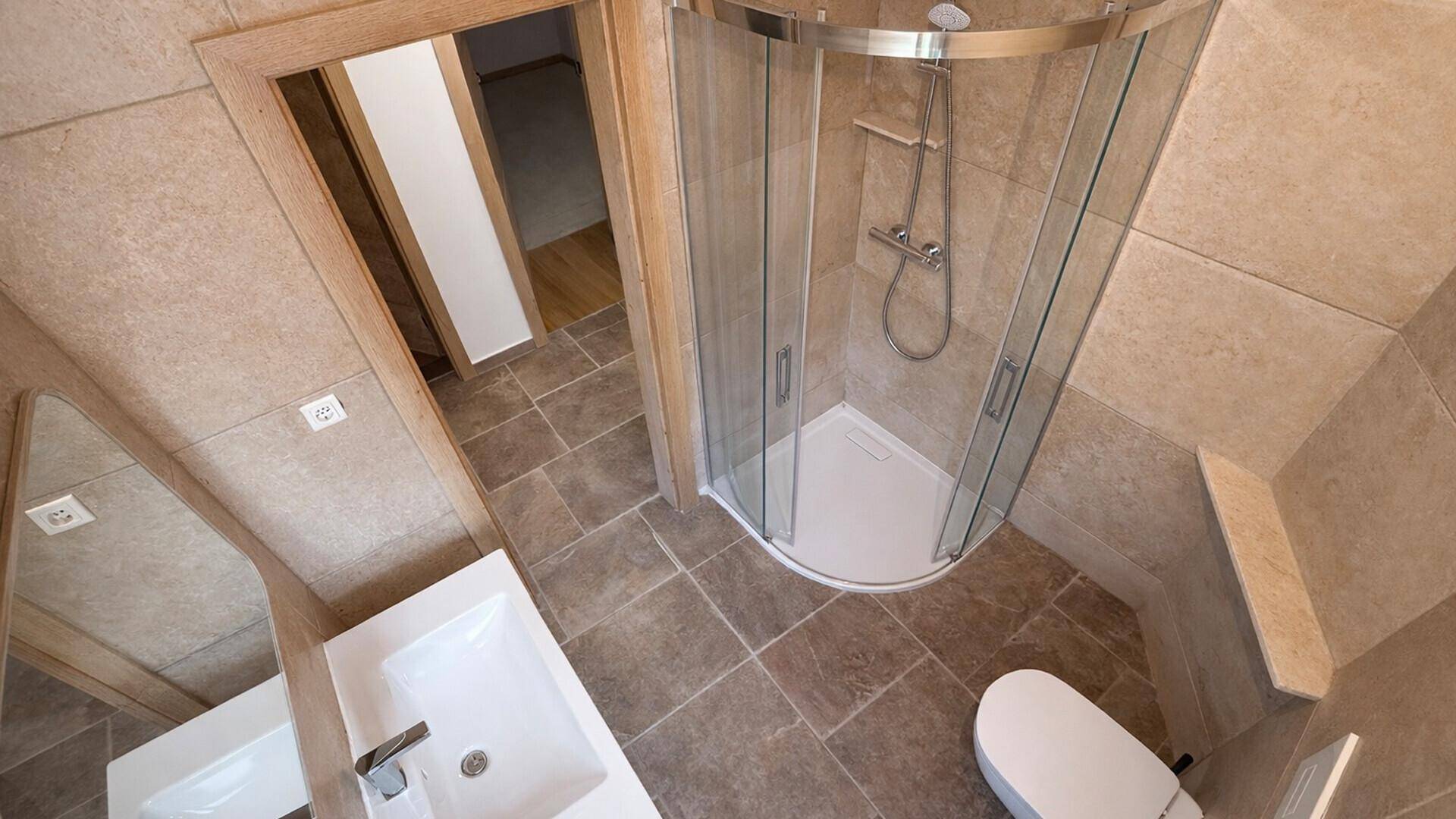 Modernes Badezimmer mit Duschkabine, Waschbecken und Wand-WC, komplett gefliest.