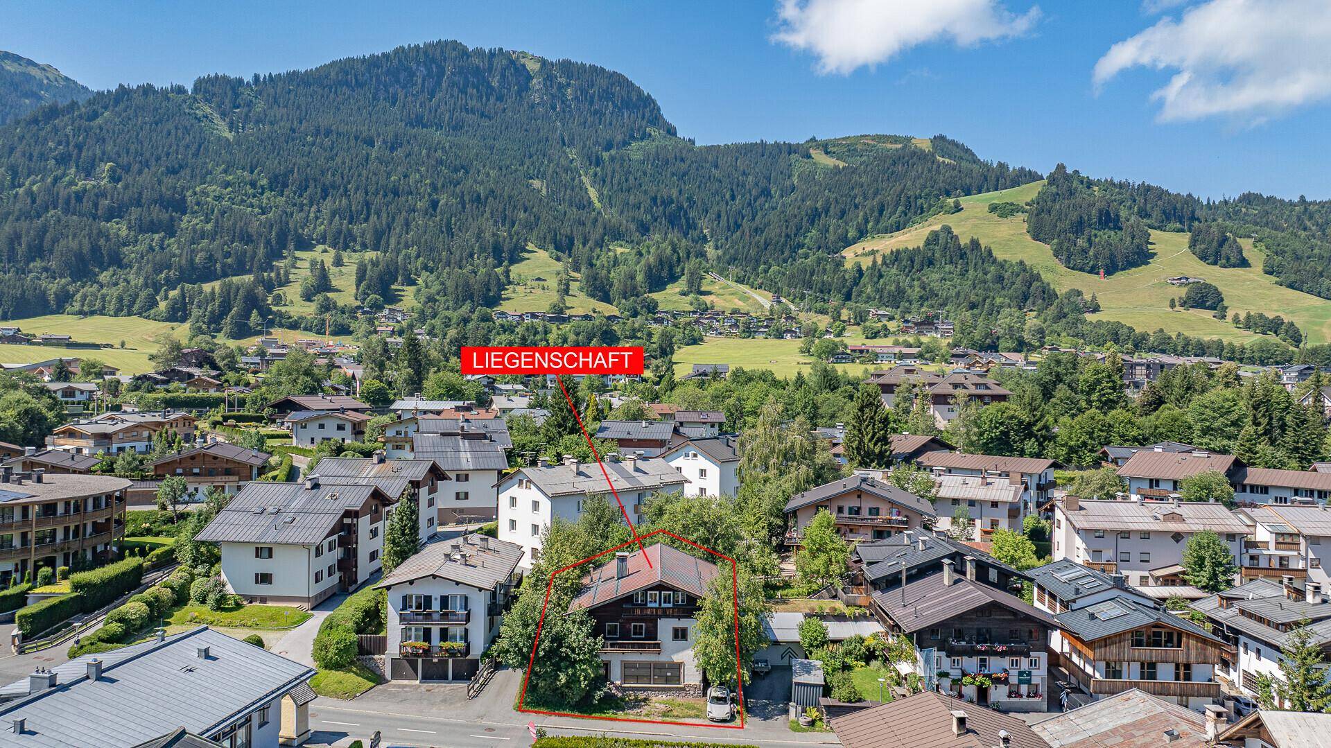 Detaillierte Luftaufnahme der Liegenschaft, umgeben von Bäumen und traditionellen Häusern in den Alpen.
