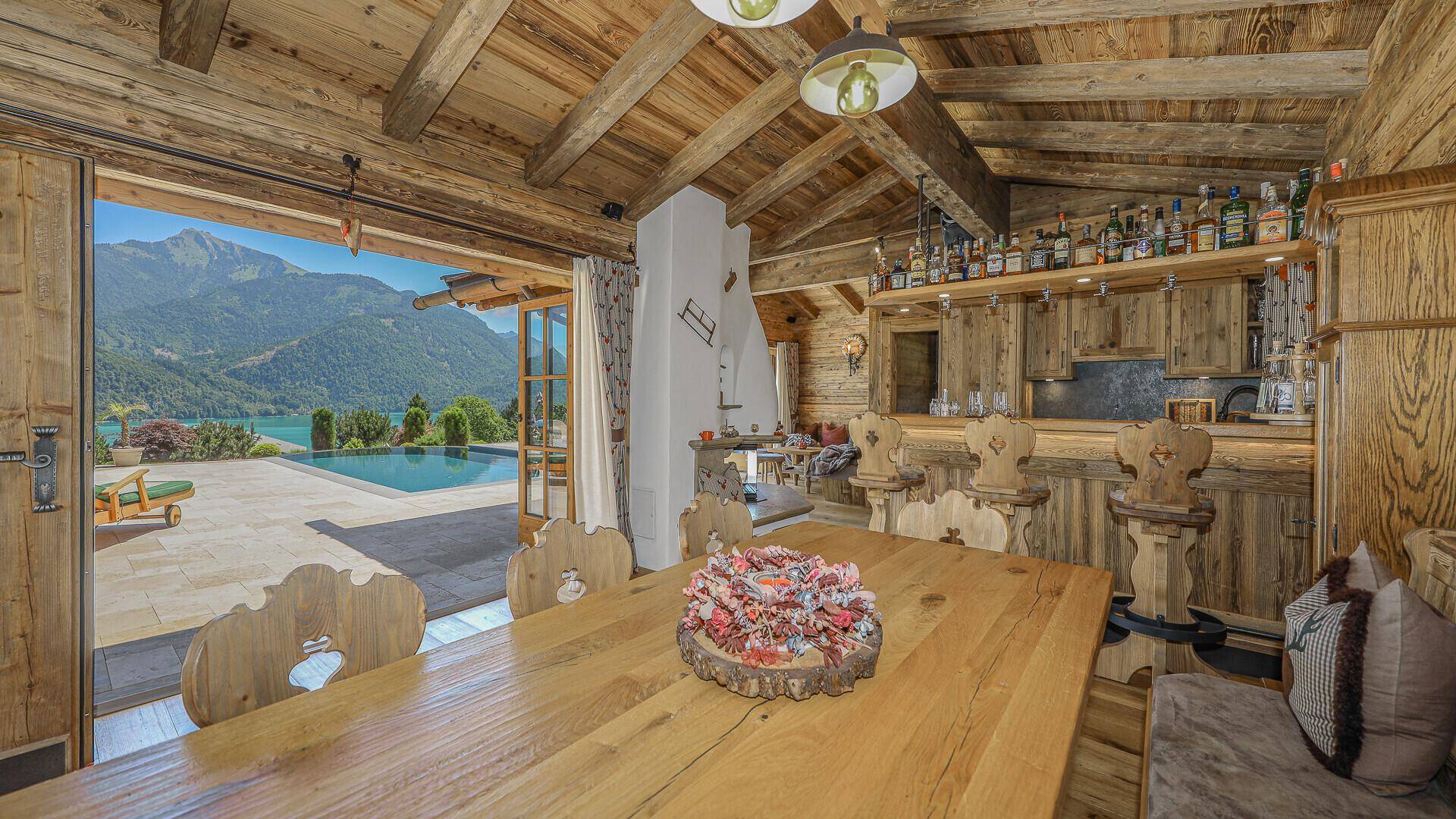 Rustikaler Essbereich im Holzhaus mit Bar, Holztisch und Blick auf den Pool und See.