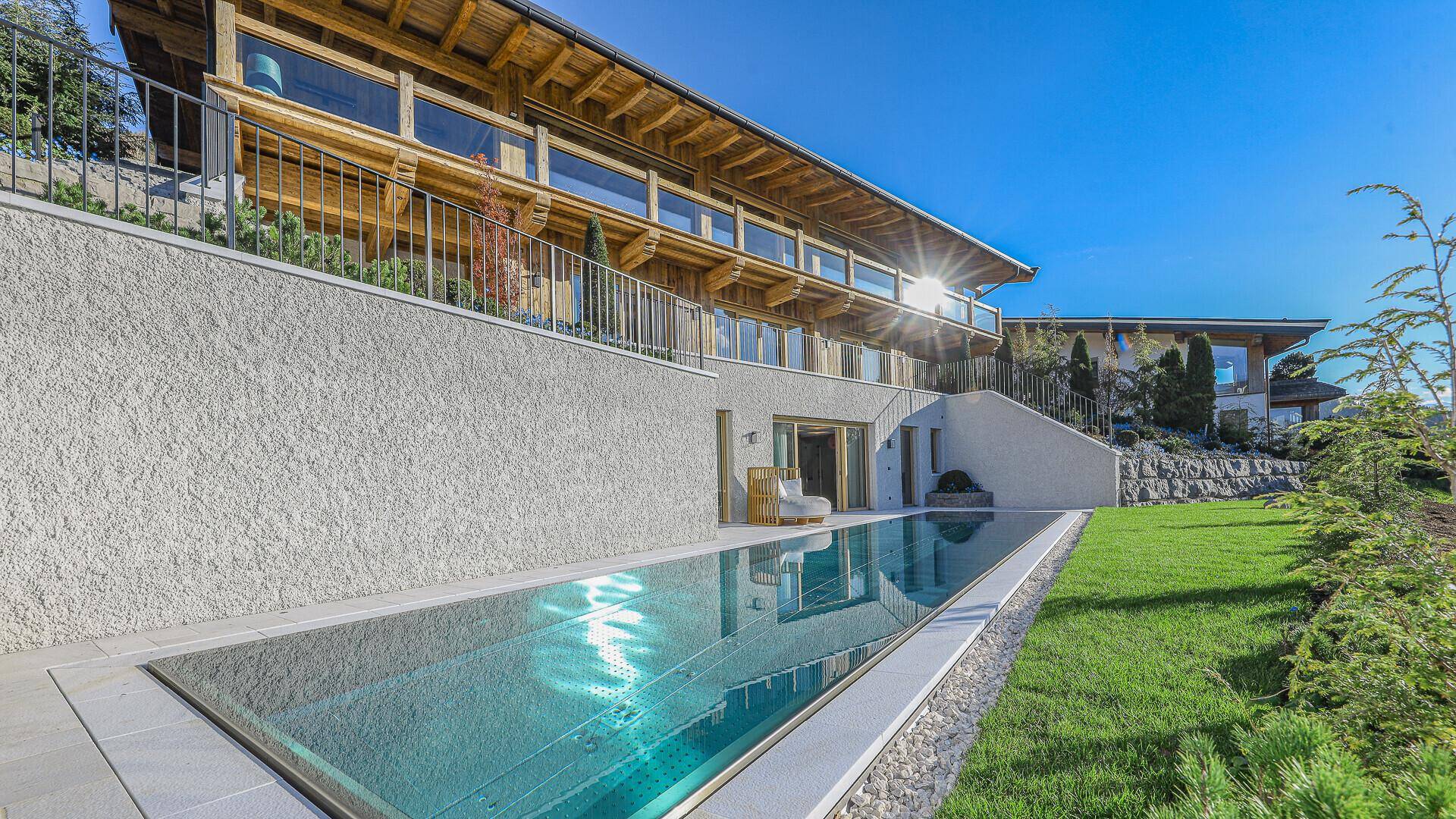 Moderne Villa mit langem Infinity-Pool und gepflegtem Gartenbereich unter strahlend blauem Himmel.