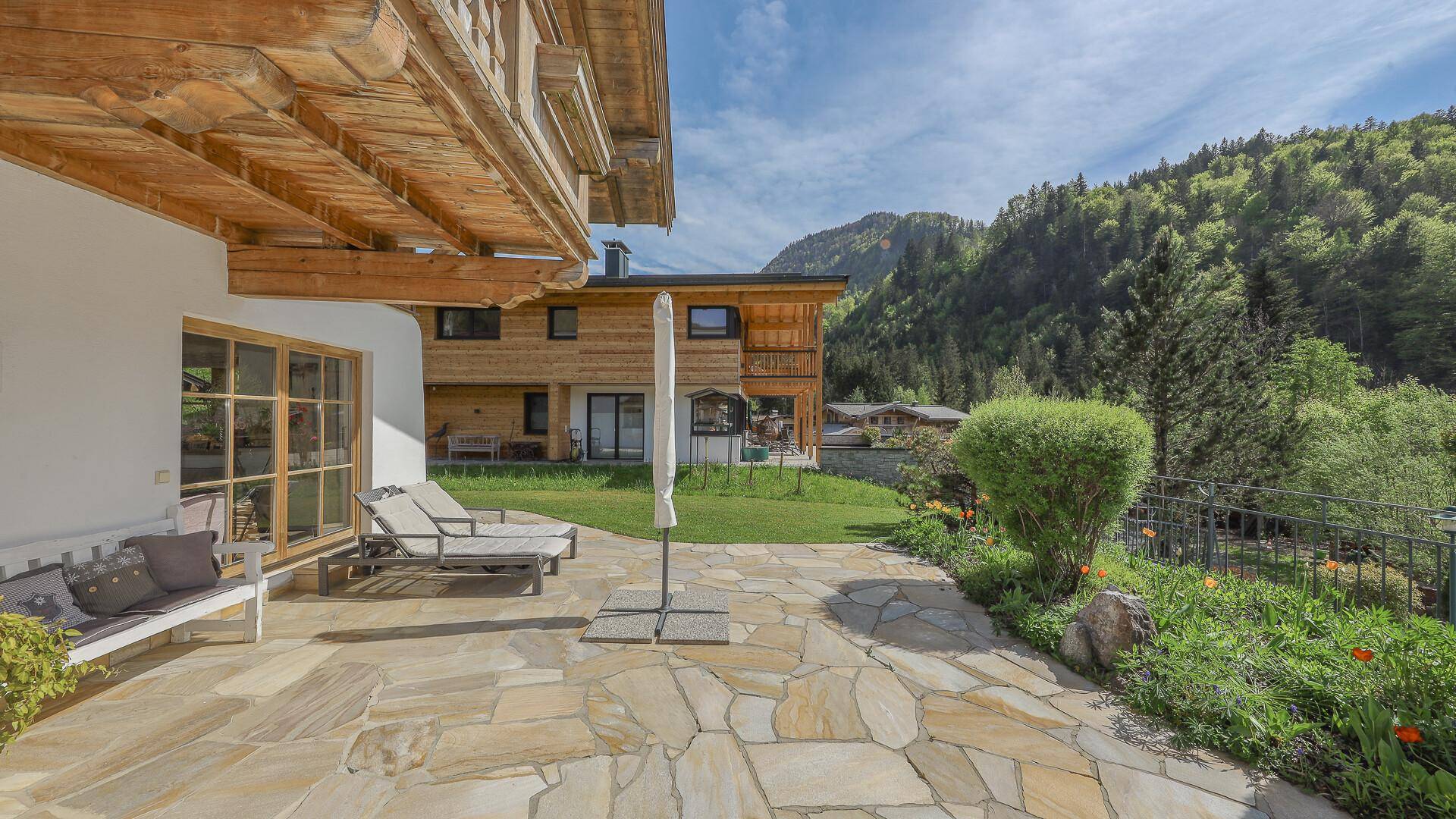 Einladende Terrasse mit Sitzgelegenheiten, Rasenfläche und Blick auf das Chalet.