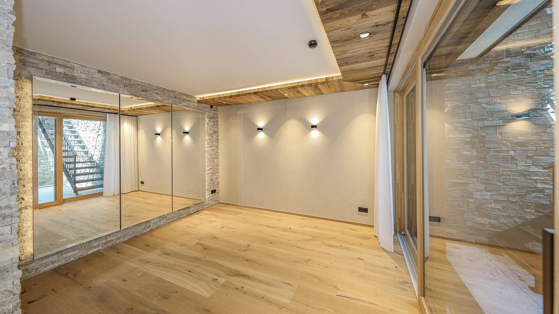 Geräumiges Schlafzimmer mit Holzboden, Spiegelfronten und Zugang zu einem Außenbereich.