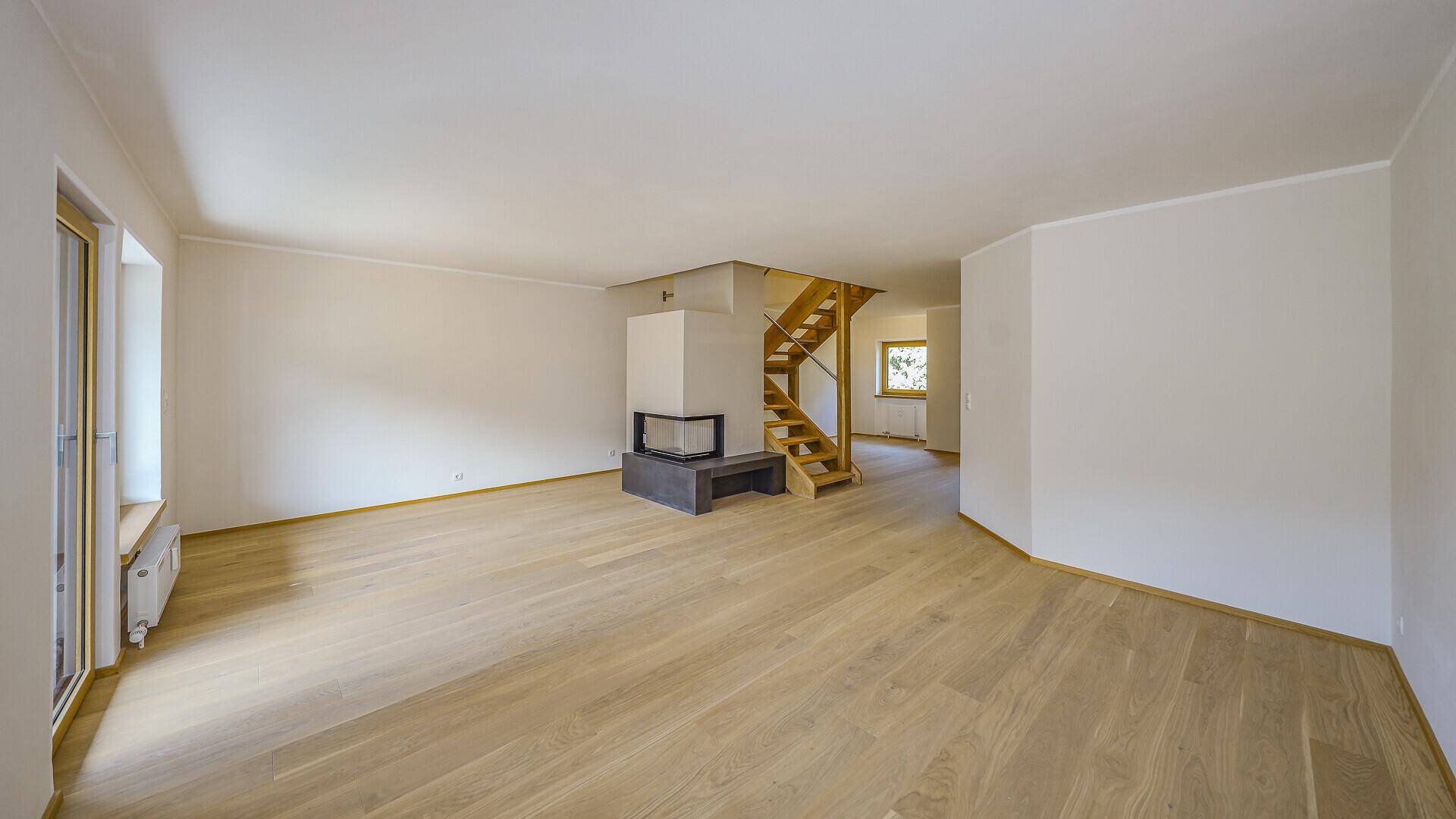 Geräumiges, unmöbliertes Wohnzimmer mit hellem Parkettboden, modernem Kamin und Holztreppe.