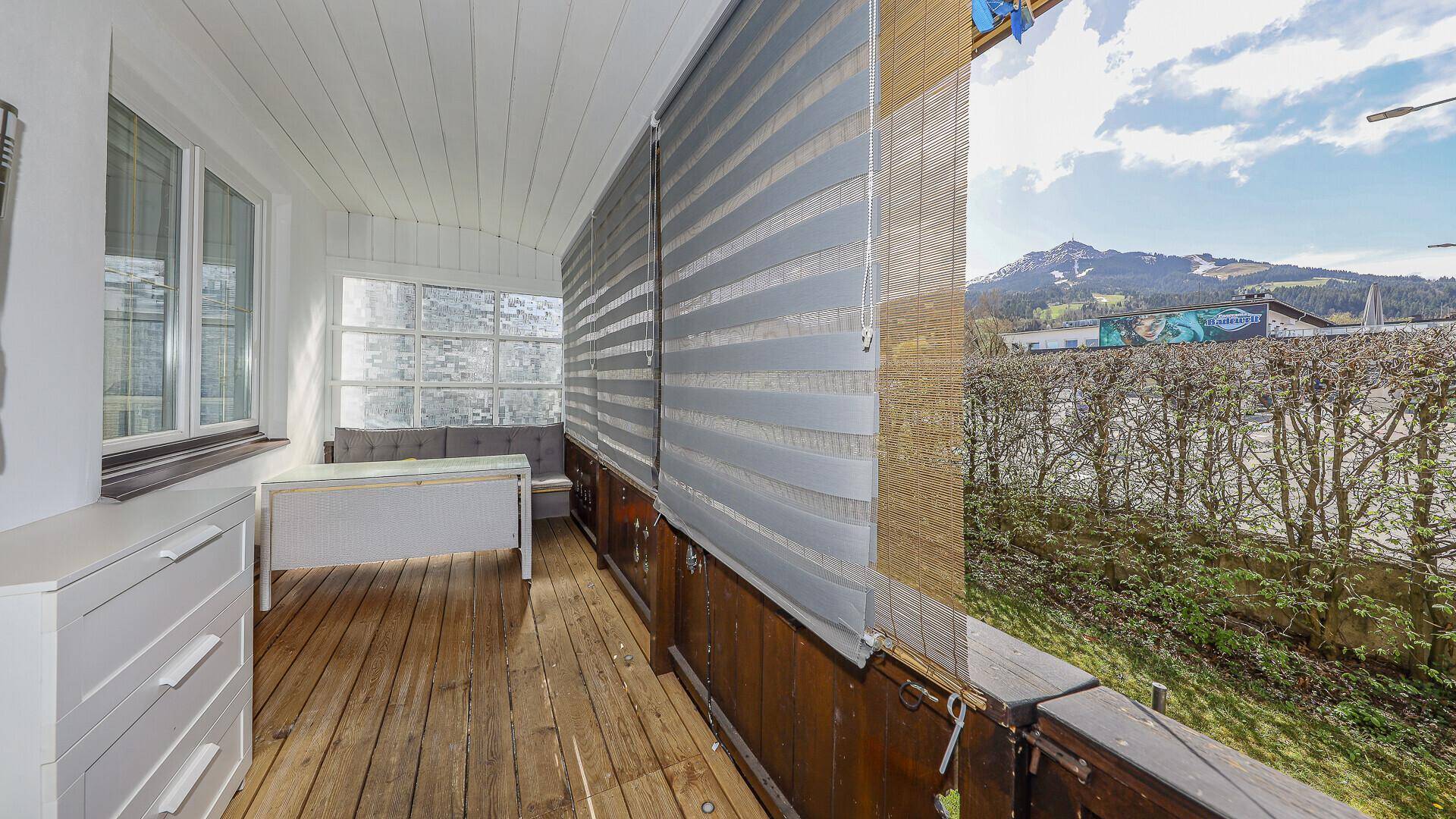 Verglaster Balkon mit Holzboden und Sitzgelegenheit, bietet einen Blick auf die Berge.