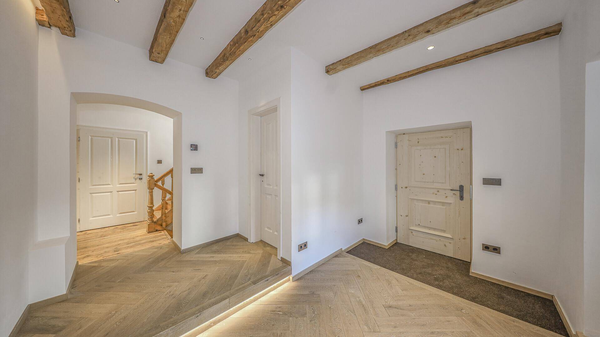 Heller Flur mit Fischgrätparkett und sichtbaren Holzbalken.
