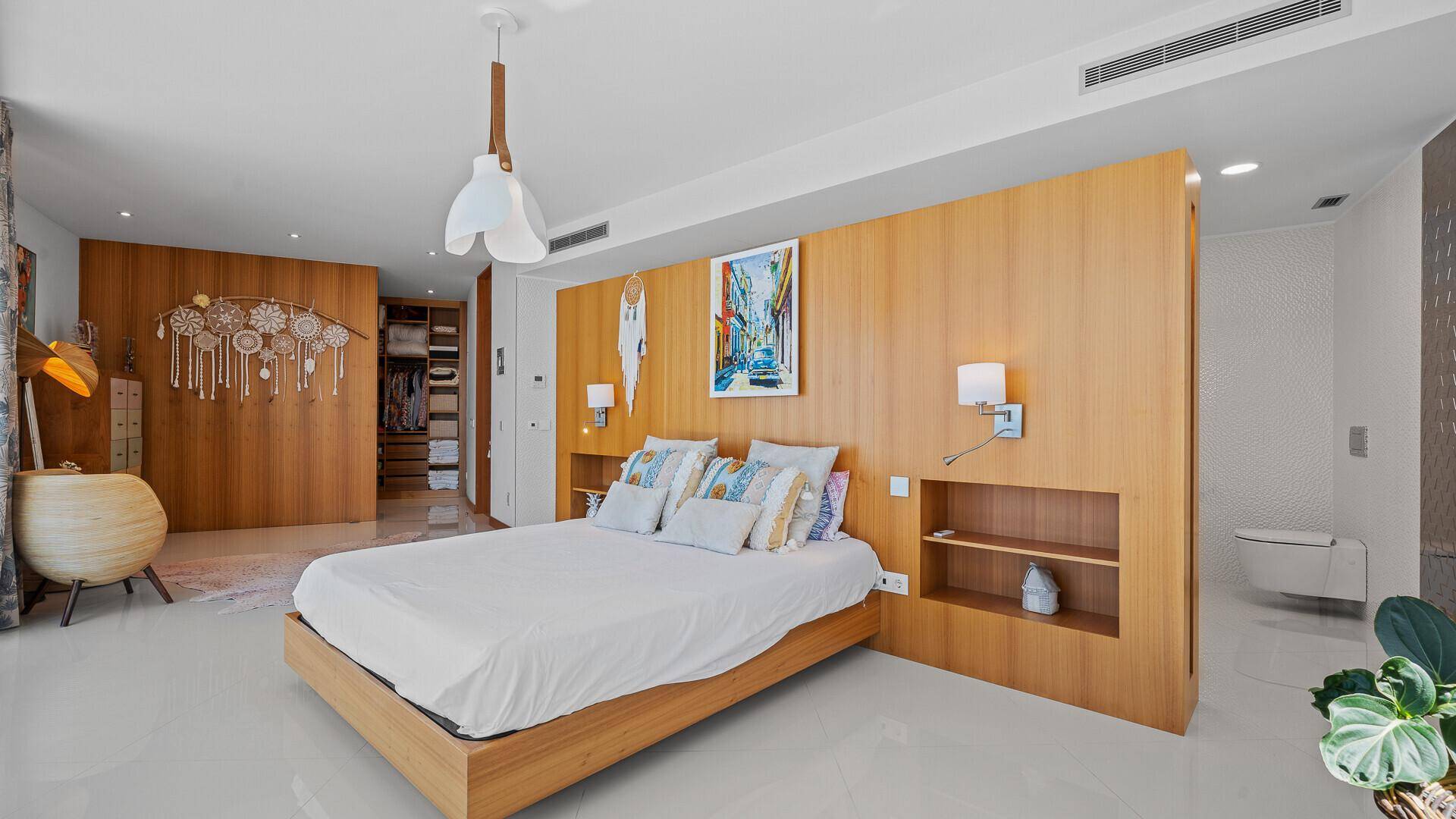 Modernes Schlafzimmer mit Holzelementen, integriertem Kopfteil und offenem Zugang zum Ankleidezimmer.