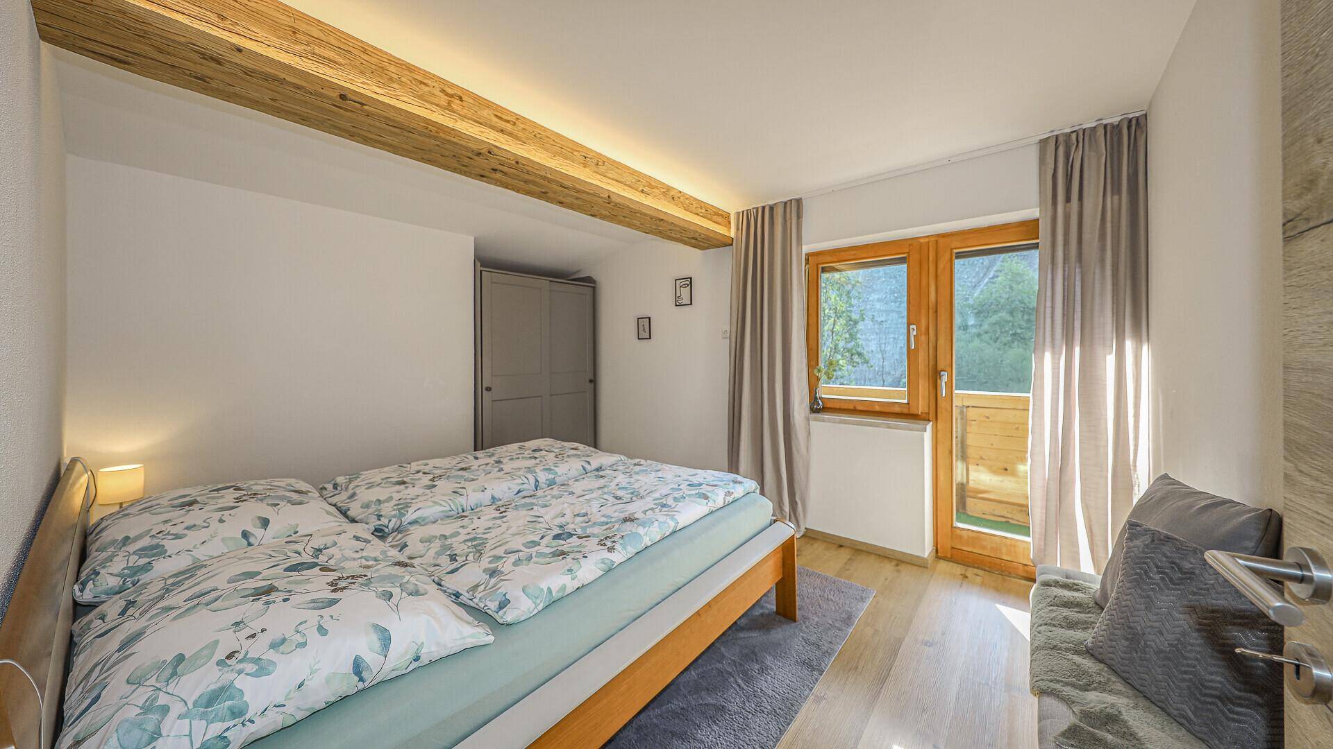 Helles Schlafzimmer mit Doppelbett, floraler Bettwäsche und direktem Zugang zu einem Balkon oder einer Terrasse.