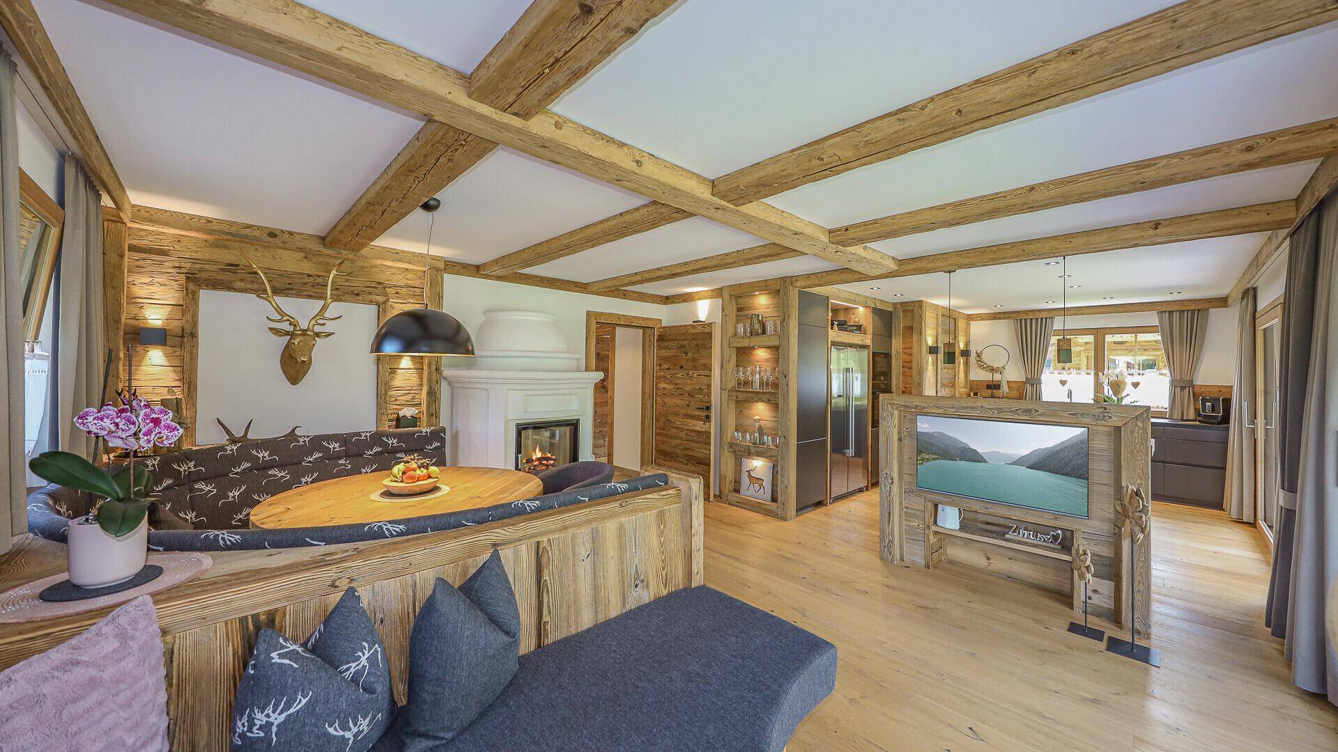 Gemütliches Wohnzimmer im alpinen Stil mit Holzbalkendecke, Kamin und traditioneller Sitzecke.