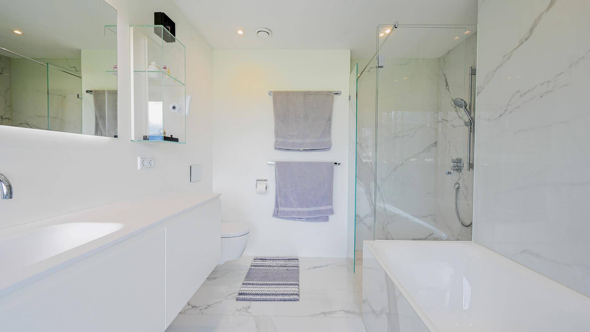 Elegantes Badezimmer mit weißen Marmorfliesen, großem Waschtisch und moderner Dusche.