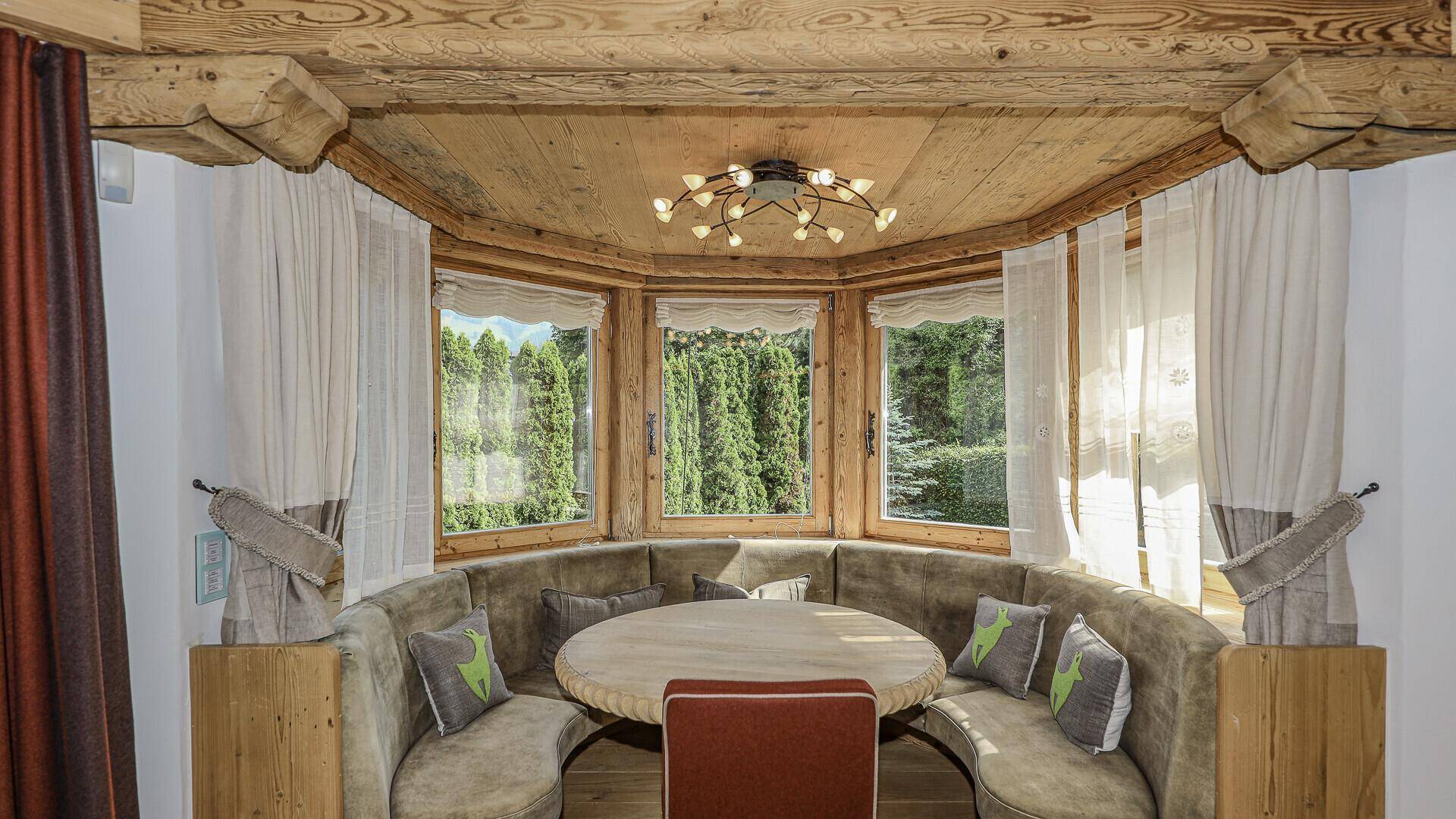 Gemütliche Essecke mit Rundbank, Holztisch und großen Fenstern mit Gartenblick.