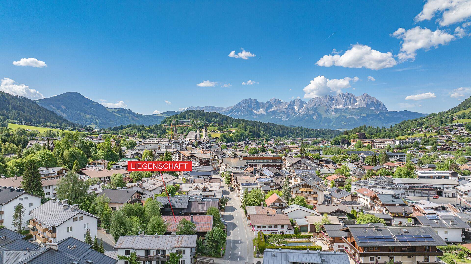 Luftaufnahme einer malerischen Alpenstadt mit markierter Liegenschaft und beeindruckendem Bergpanorama.