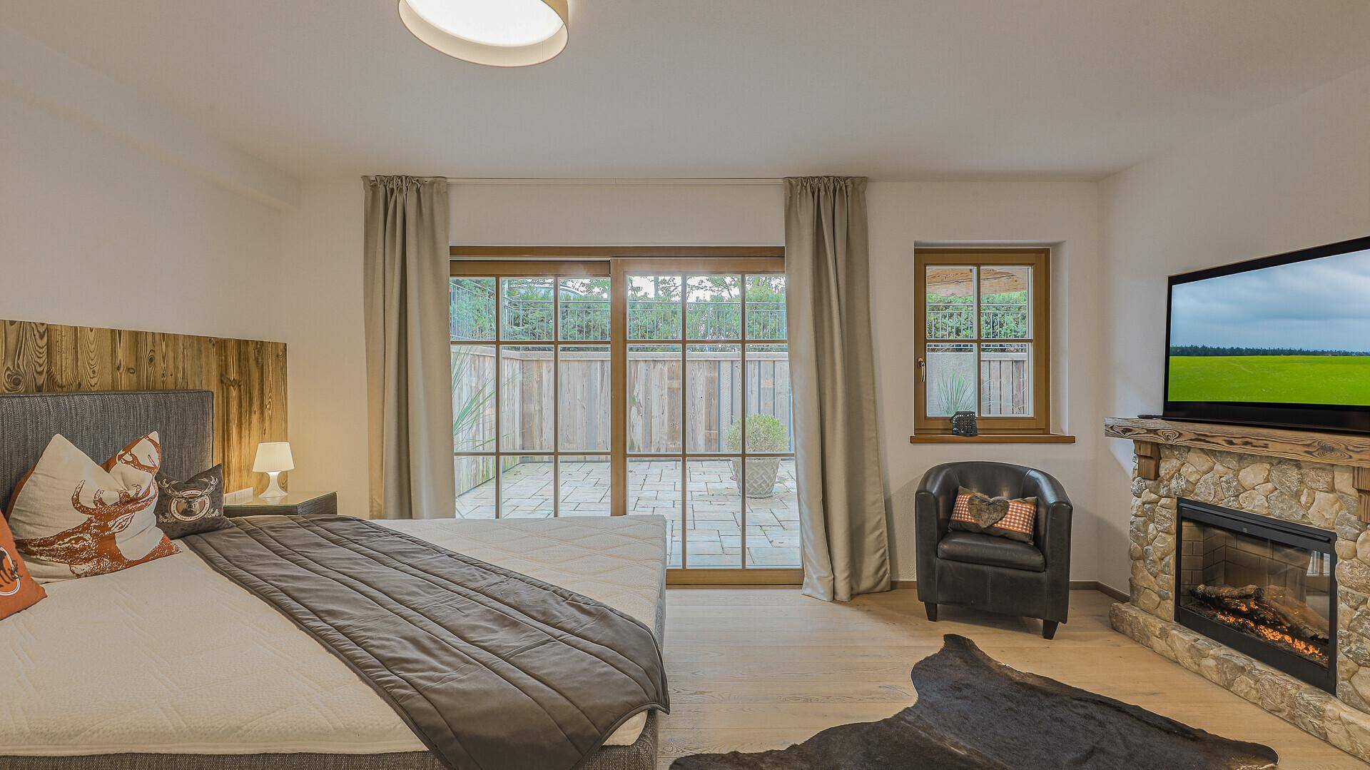 Gemütliches Schlafzimmer mit Kamin, Holzboden und direktem Zugang zur Terrasse.