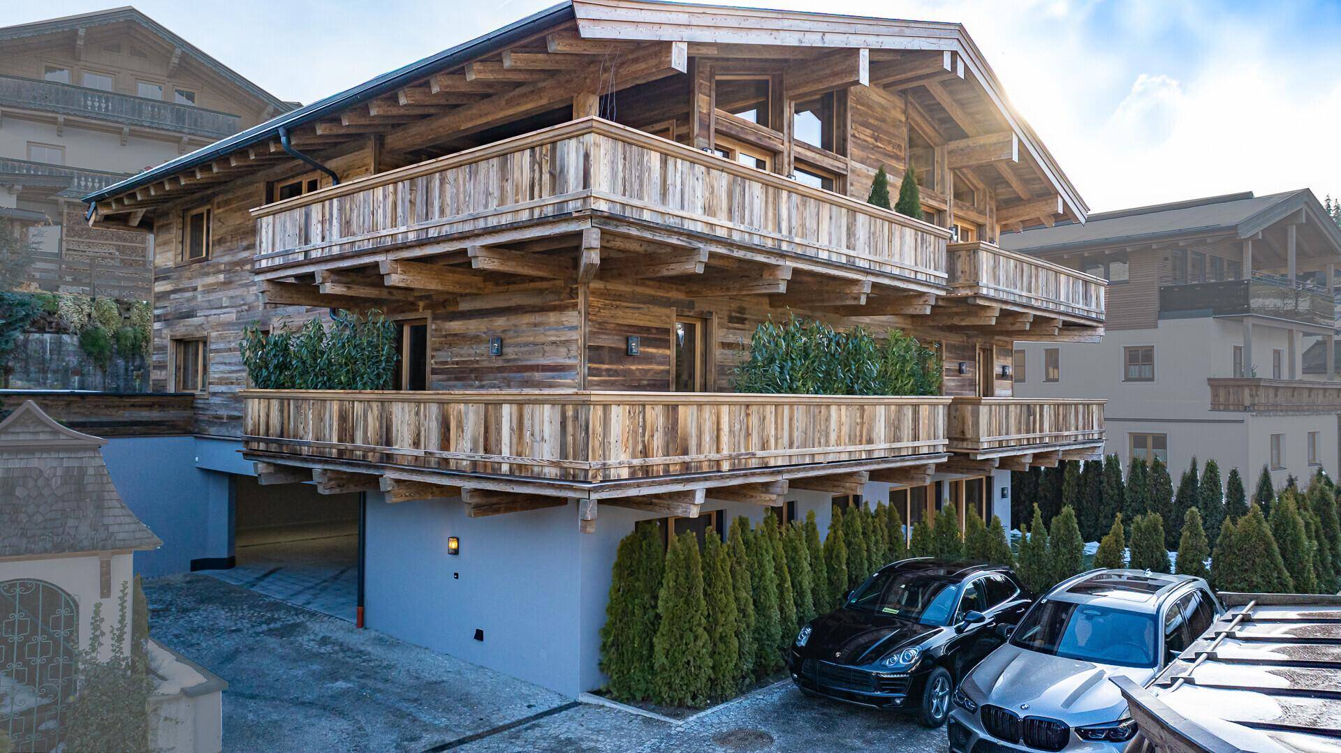 Elegantes Chalet mit Holzfassade, Balkonen und Stellplätzen im Freien.