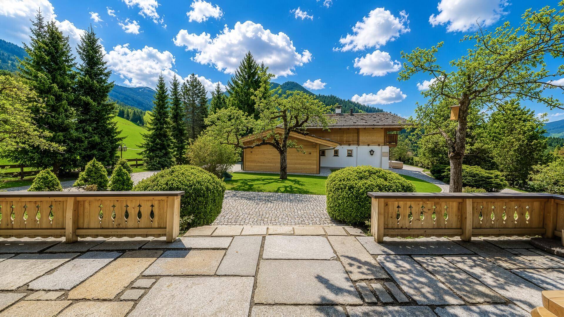 Großer Gartenbereich mit gepflasterter Terrasse, Obstbäumen und Blick auf die Berge.