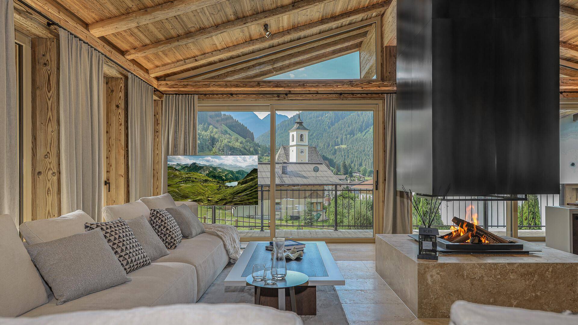 Helles Wohnzimmer mit großem Sofa, Kamin und weitem Blick auf die umliegende Berglandschaft.