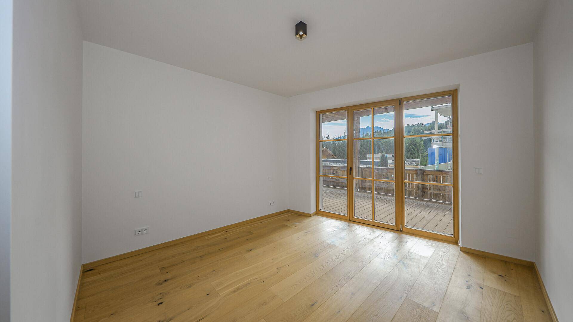 Helles Zimmer mit Holzboden und Zugang zu einem Balkon mit Bergblick.
