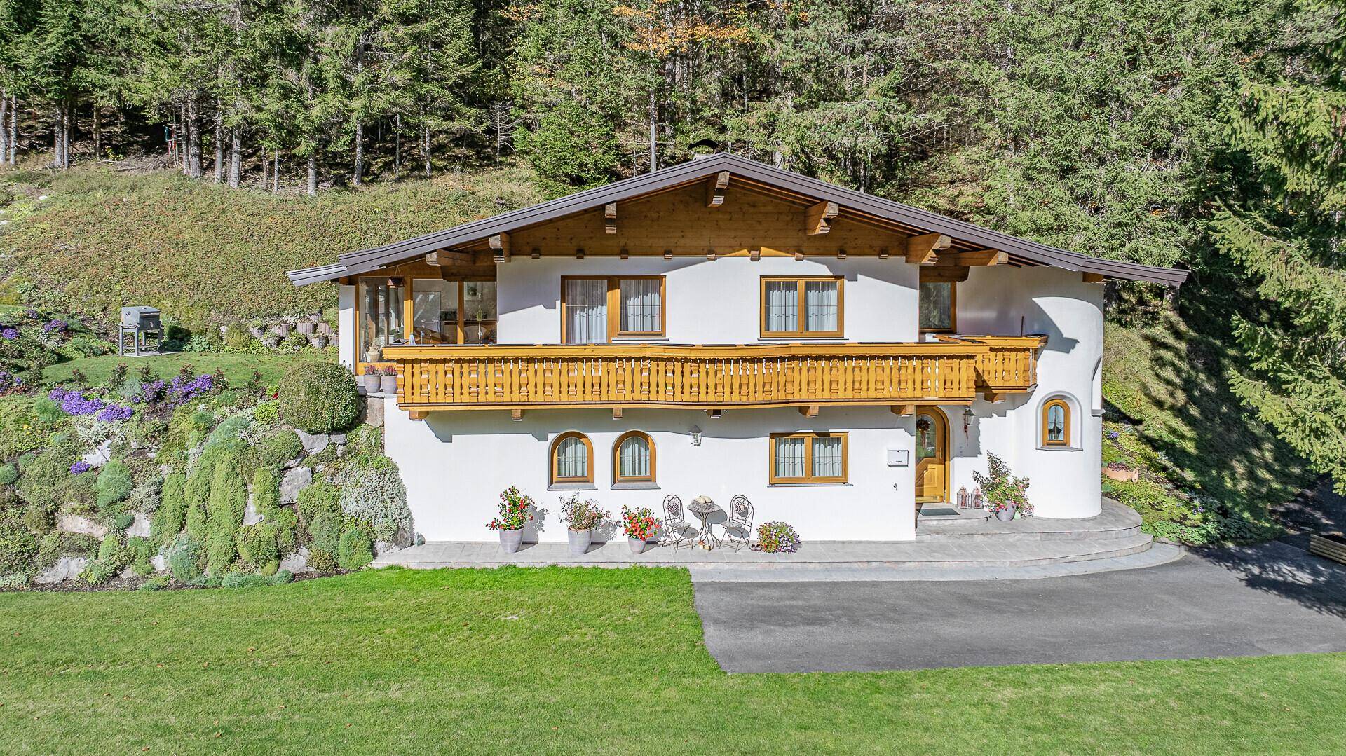 Traditionelles Alpenchalet mit weißer Fassade, Holzbalkonen und gepflegtem Vorgarten in sonniger Lage.