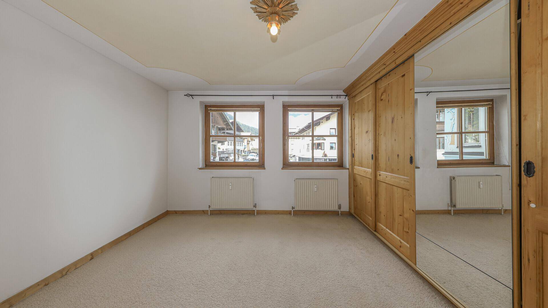 Helles Schlafzimmer mit Teppichboden, Holzschränken und Blick auf die umliegenden Häuser.