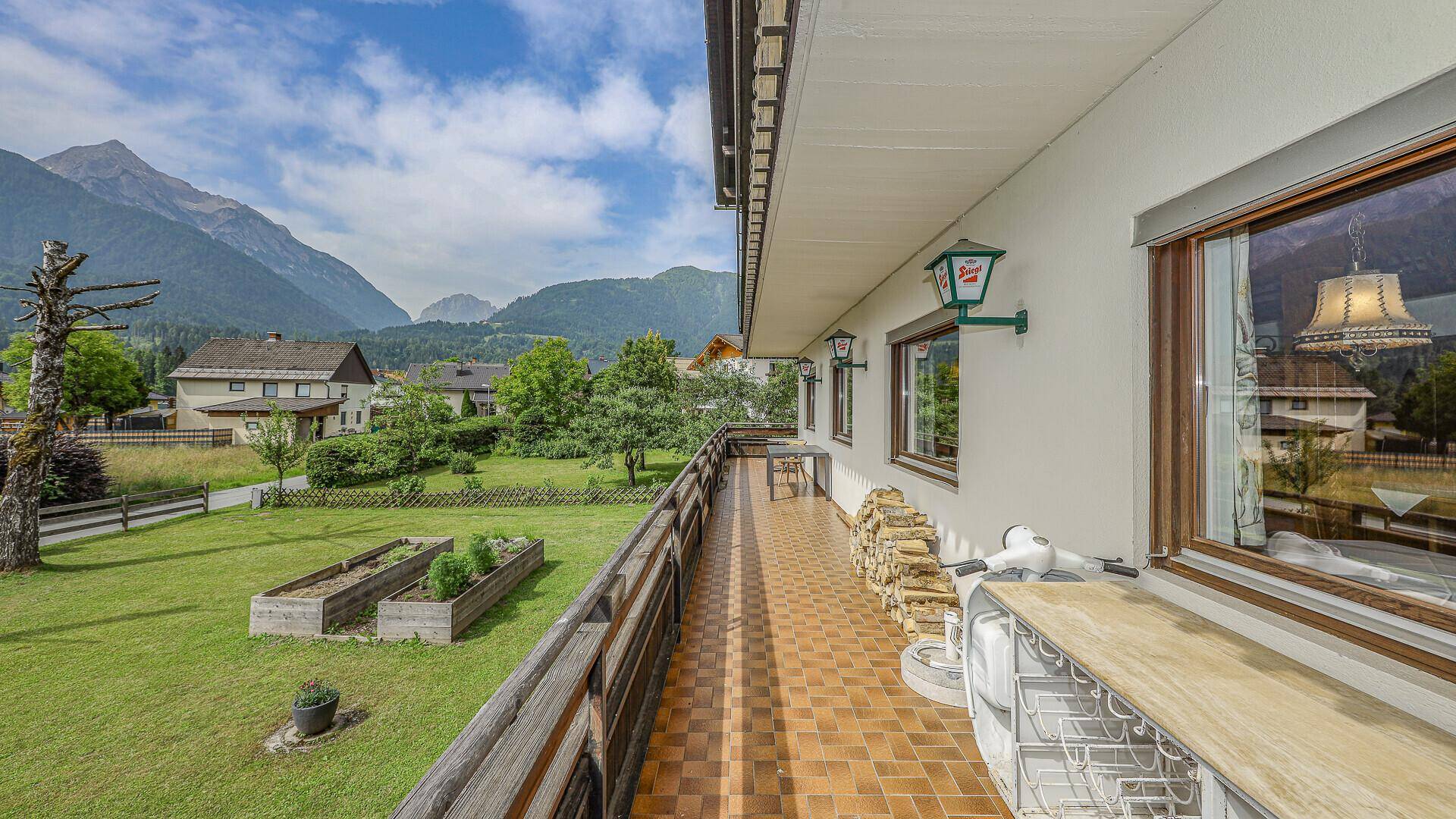 Geräumiger Balkon mit Holzgeländer, Fliesenboden und weitem Blick auf die Berge.