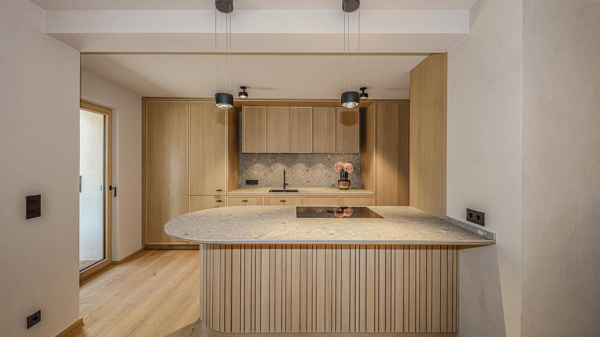 Moderne Küche mit Holzfronten, Kücheninsel und Induktionskochfeld, offen zum Wohnbereich.